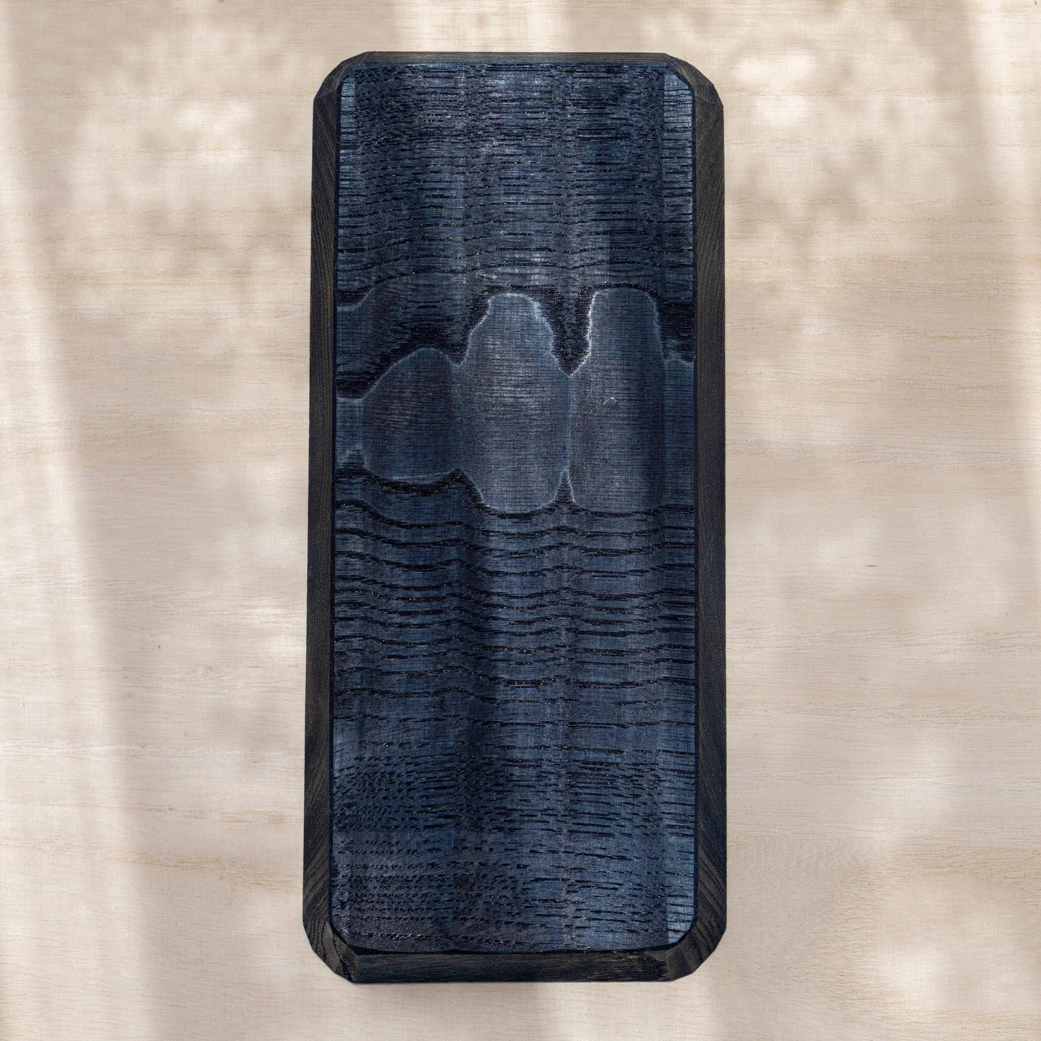 Back of indigo dyed slim chestnut pen tray, flat surface with visible wood grain and rounded corners