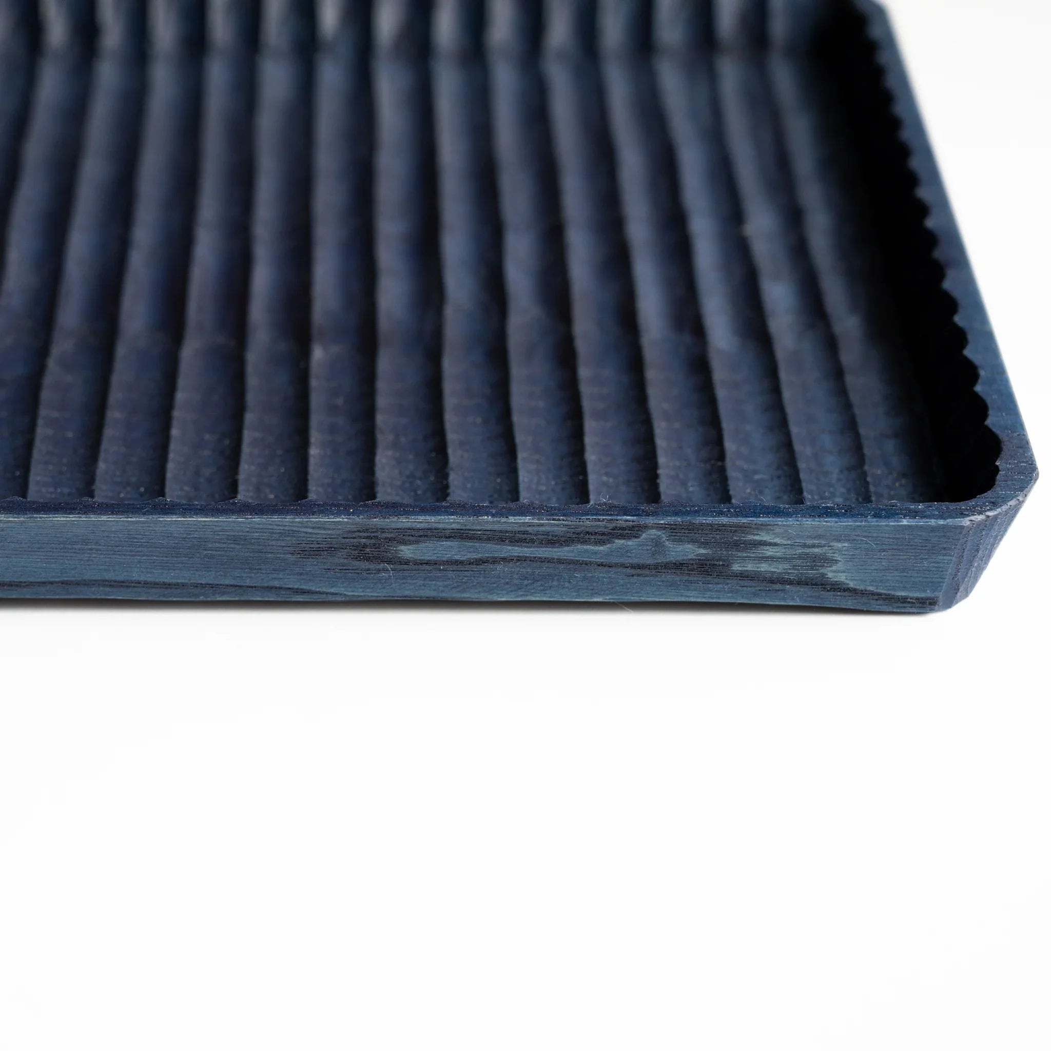 Angled view of indigo dyed chestnut pen tray showing carved grooves, scalloped rim and the thickness of the side