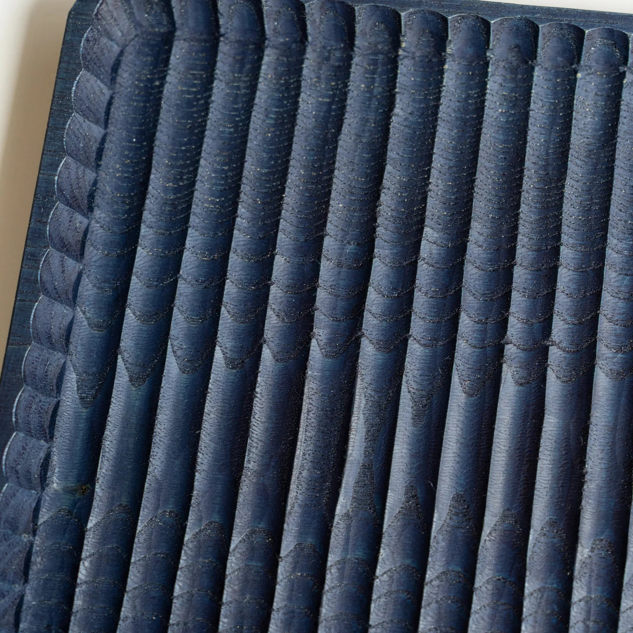 Close-up of indigo dyed chestnut showing chisel marks along the carved ridges, with paler blue on the ridge tops