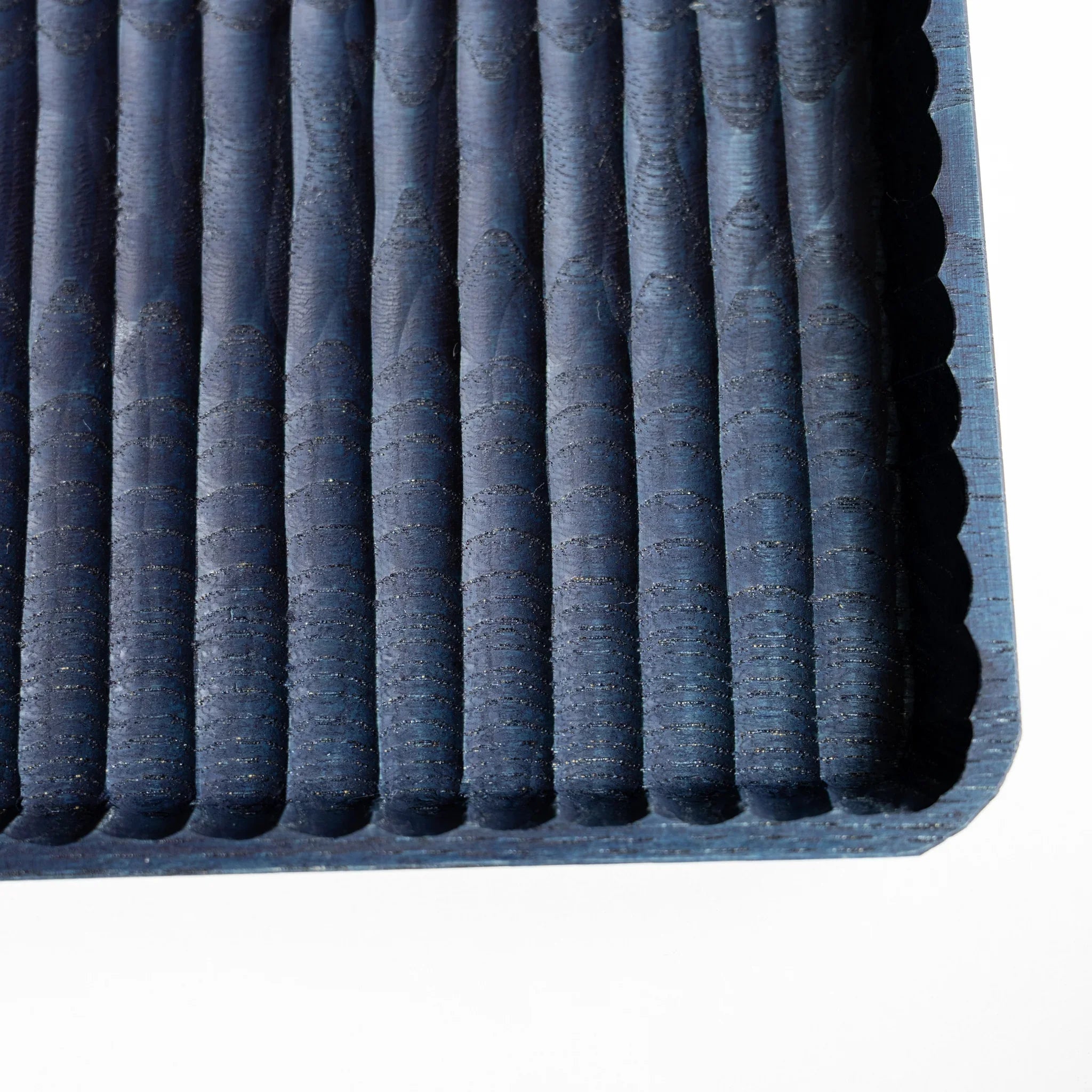 Close-up of the corner of an indigo dyed chestnut pen tray where the carved grooves meet the scalloped rim