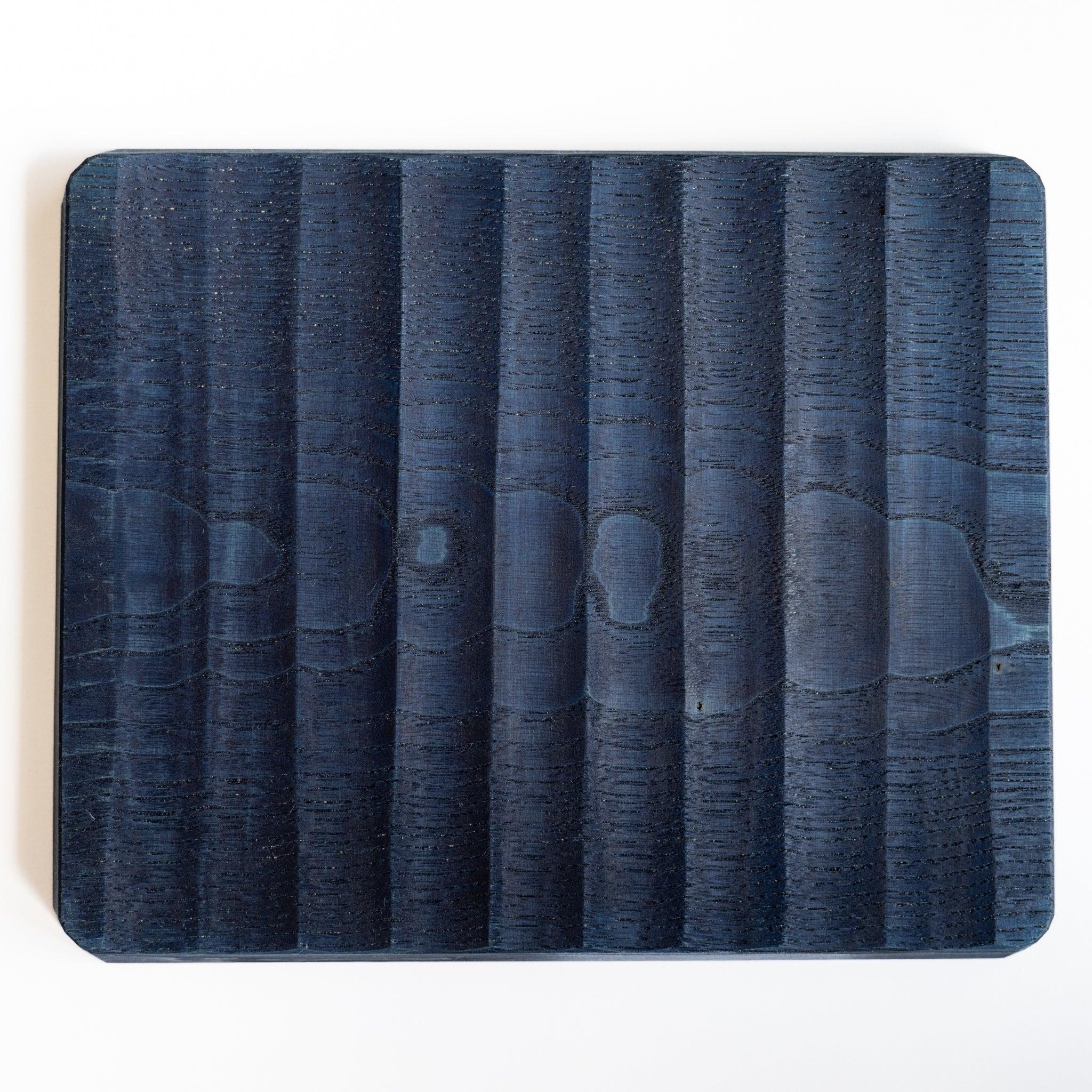 Back of indigo dyed wide chestnut pen tray, broad carved facets across a flat surface with rounded corners