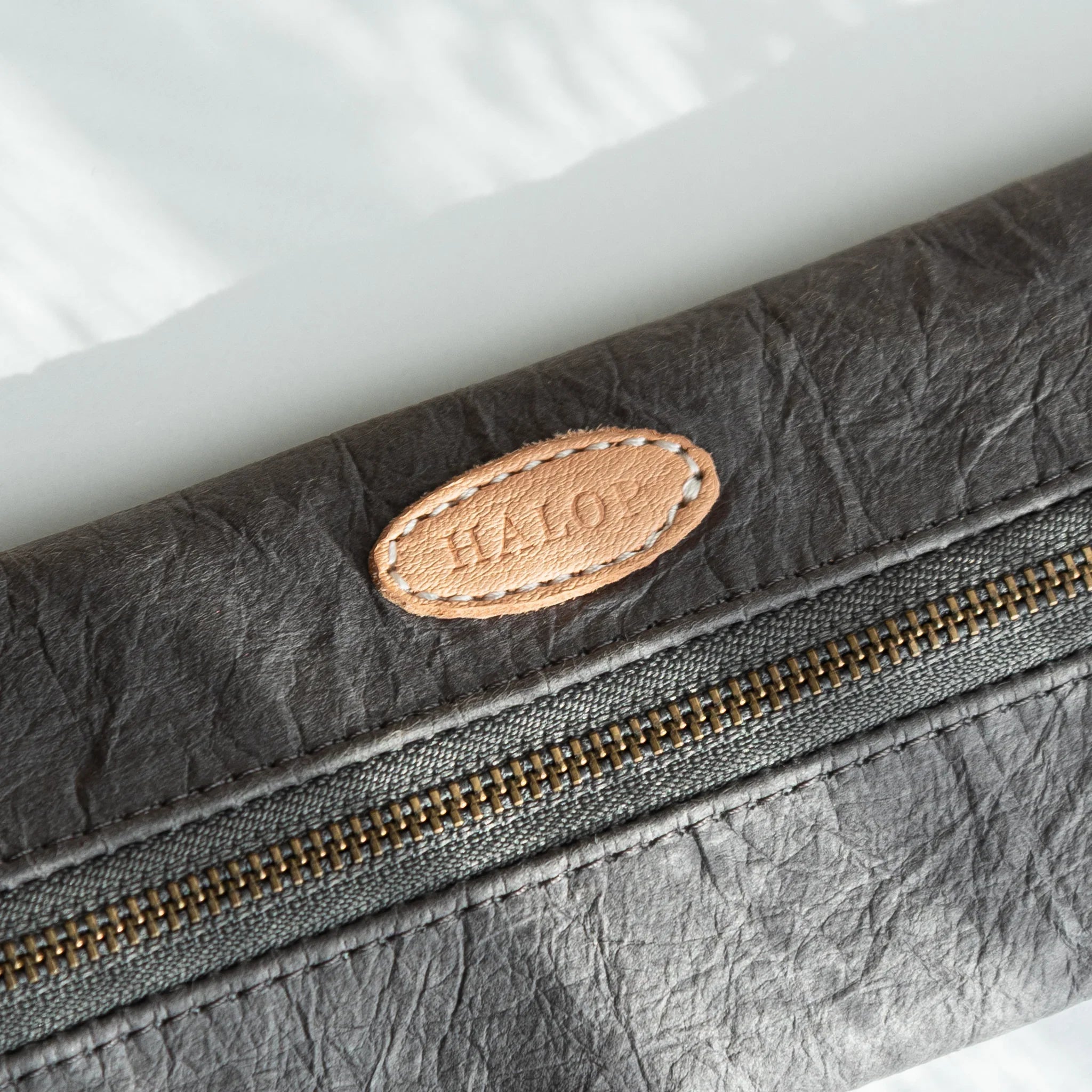 Close-up of the brass zipper and leather ring of the grey Japanese Pen Case, showing the washi paper’s soft wrinkles.