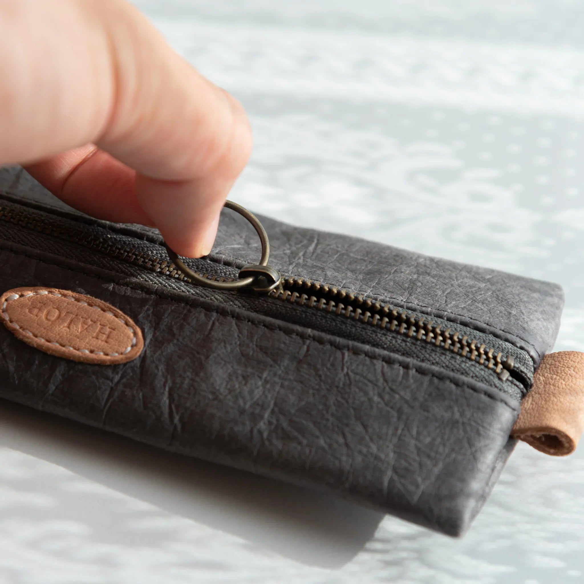 Hand opening the handcrafted Japanese Pen Case using the round metal zipper ring, emphasizing artisanal craftsmanship.