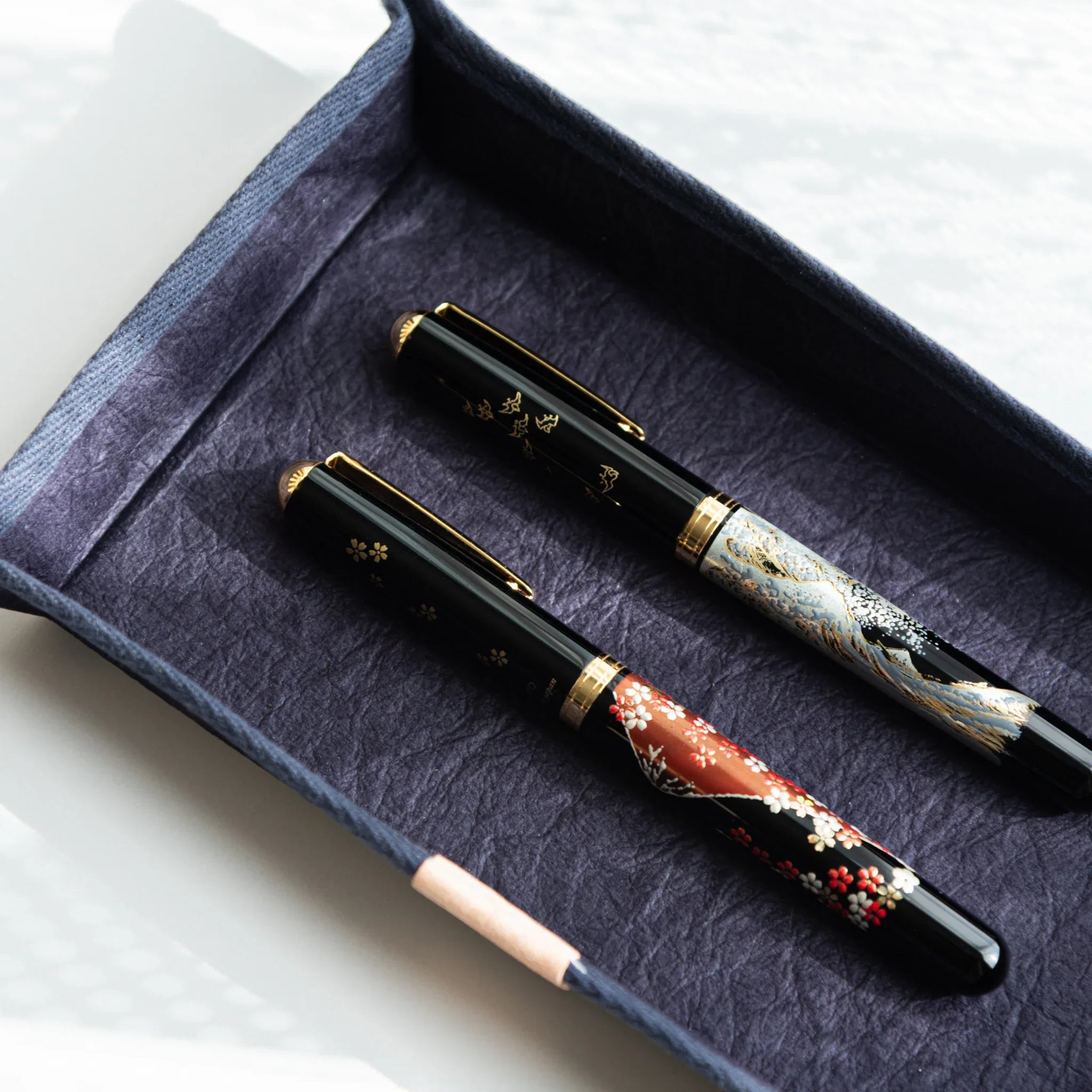 Close-up of two lacquered Japanese Fountain Pens resting in a Handcrafted Sugihara Washi Paper Japanese purple Pen Tray.