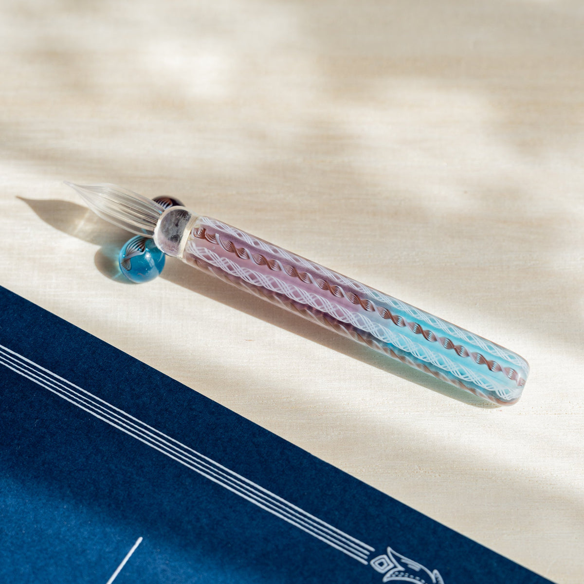Helix Dawn glass dip pen on pale wood, clear fluted nib and barrel of turquoise, pink and white lattice canes