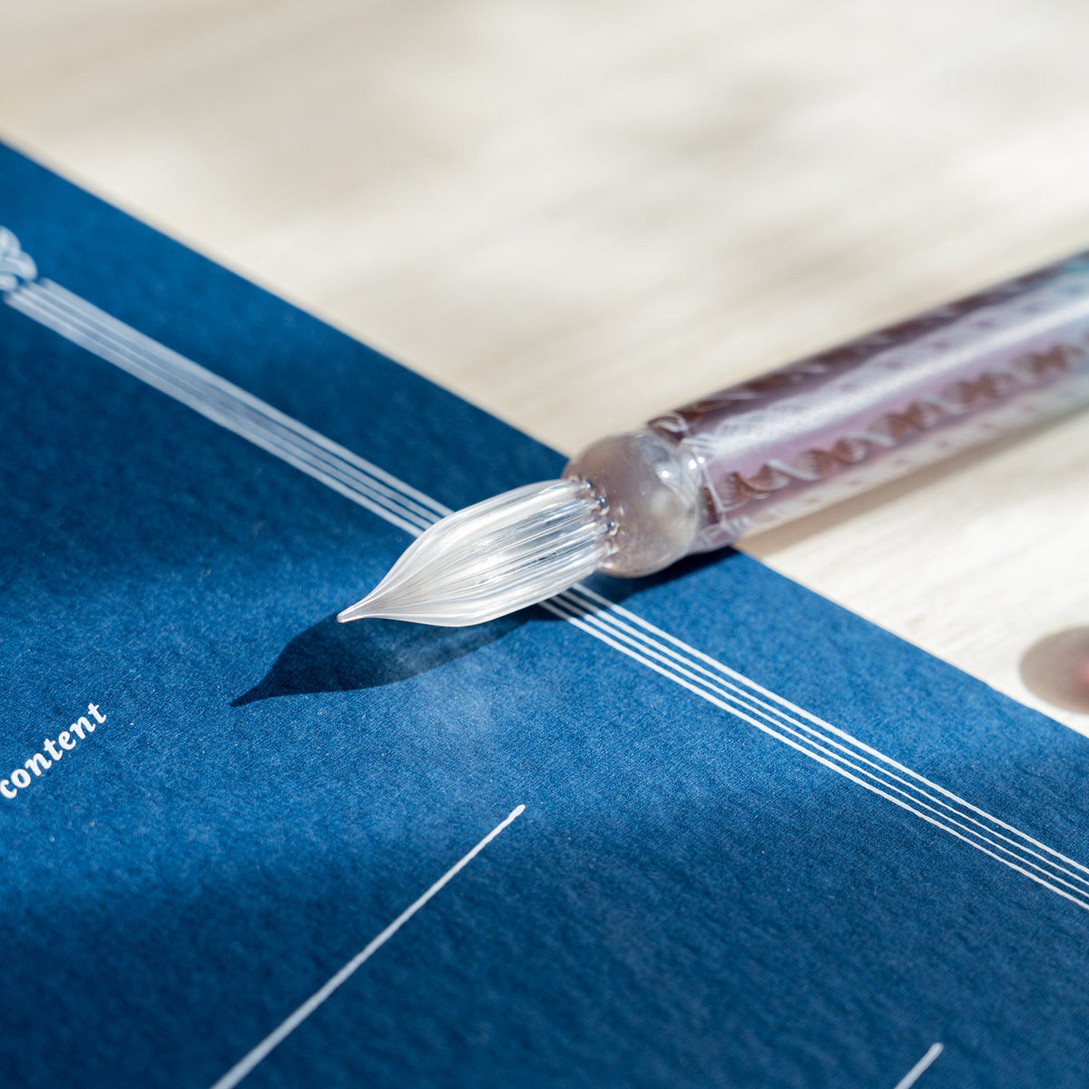 Clear fluted nib of the Helix Dawn glass dip pen resting over a printed navy blue sheet