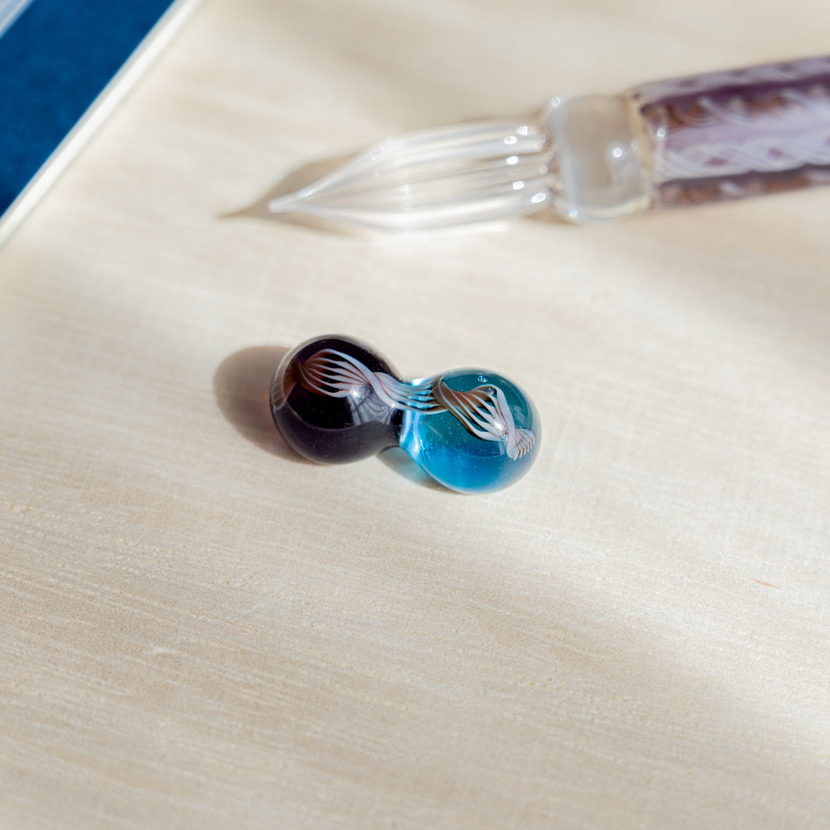 Two-sphere glass pen rest in brown and turquoise with white fan motifs, Helix Dawn nib behind