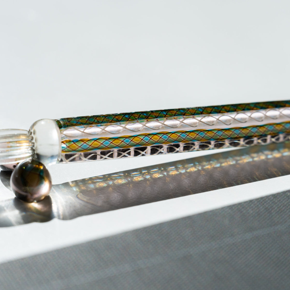 Detail of the Helix Peacock glass canes in teal, gold and white running the length of the barrel