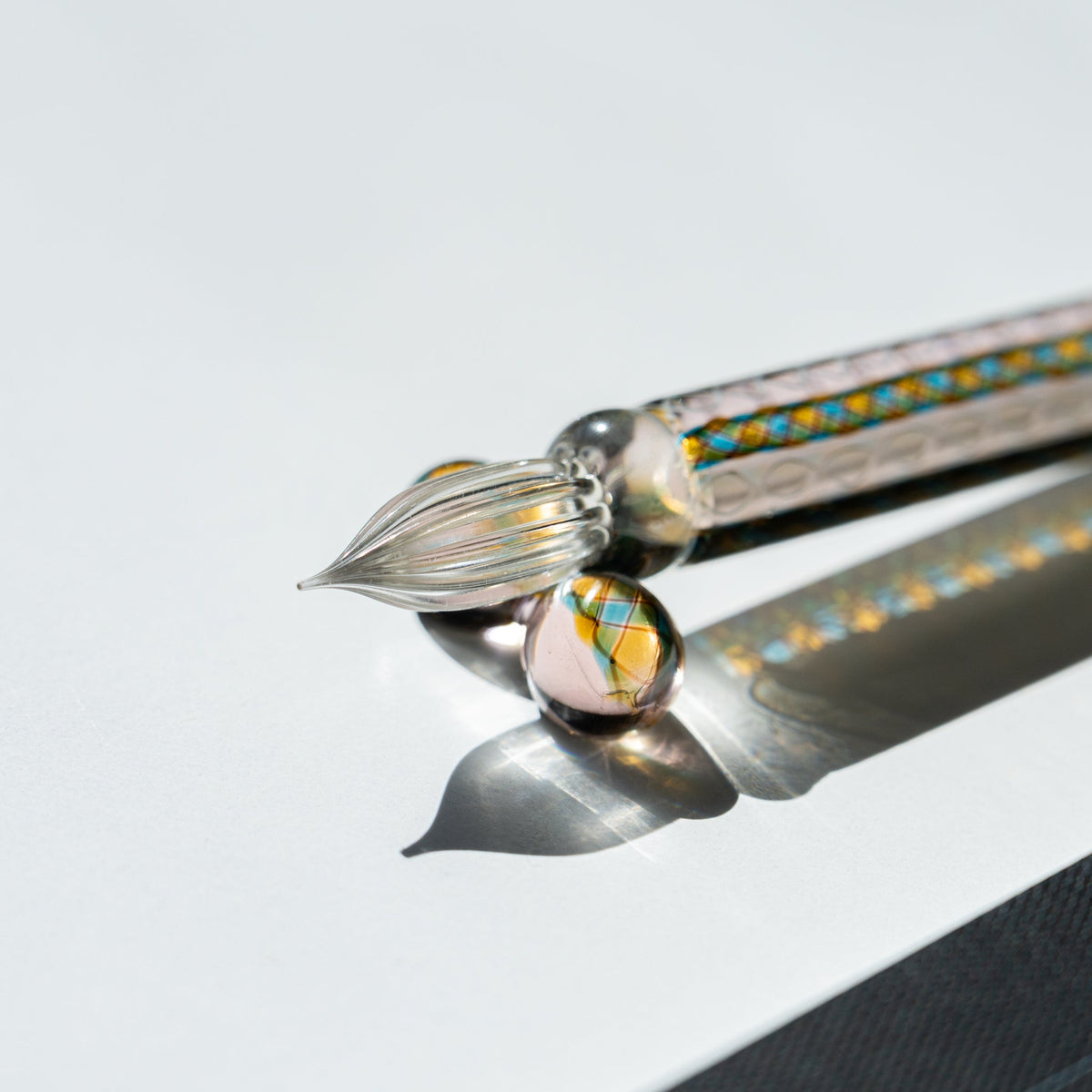 Clear fluted nib of the Helix Peacock glass dip pen with a patterned glass sphere beneath it