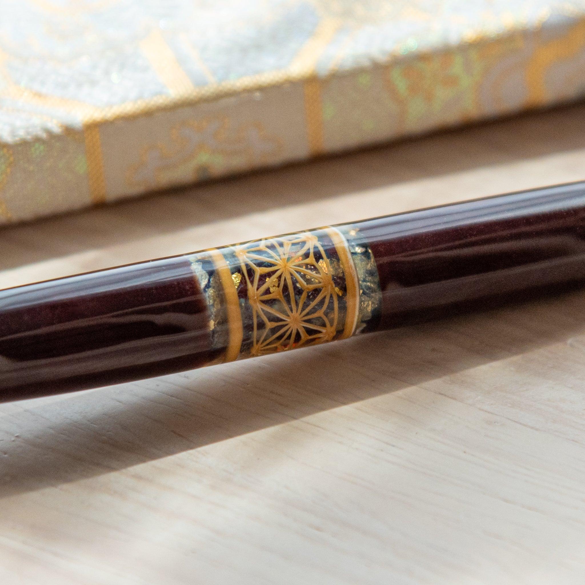 Dark brown glass pen featuring a traditional Hemp Leaves pattern in gold, paired with a matching glass pen rest. Displayed on a wooden surface with a Nishijin textile notebook.