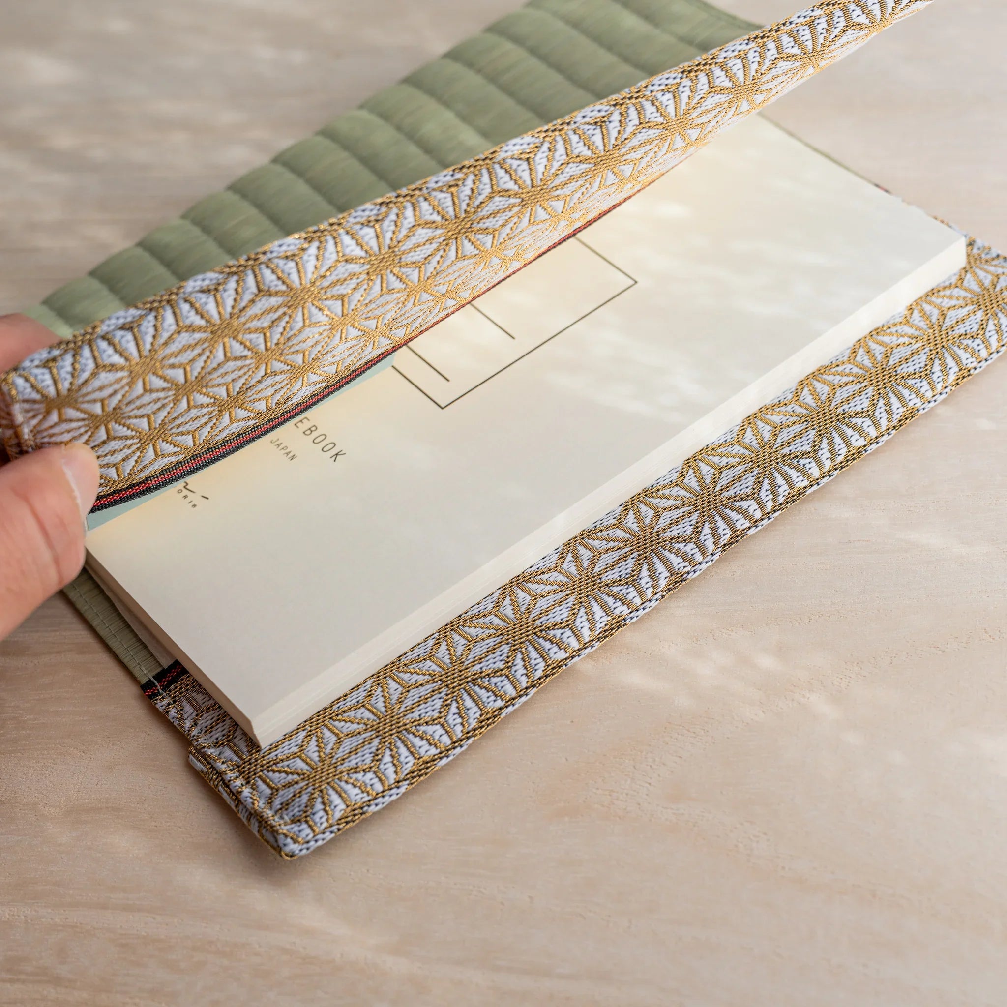Hand lifting the hemp leaf fabric flap over a notebook back cover held inside the tatami book cover