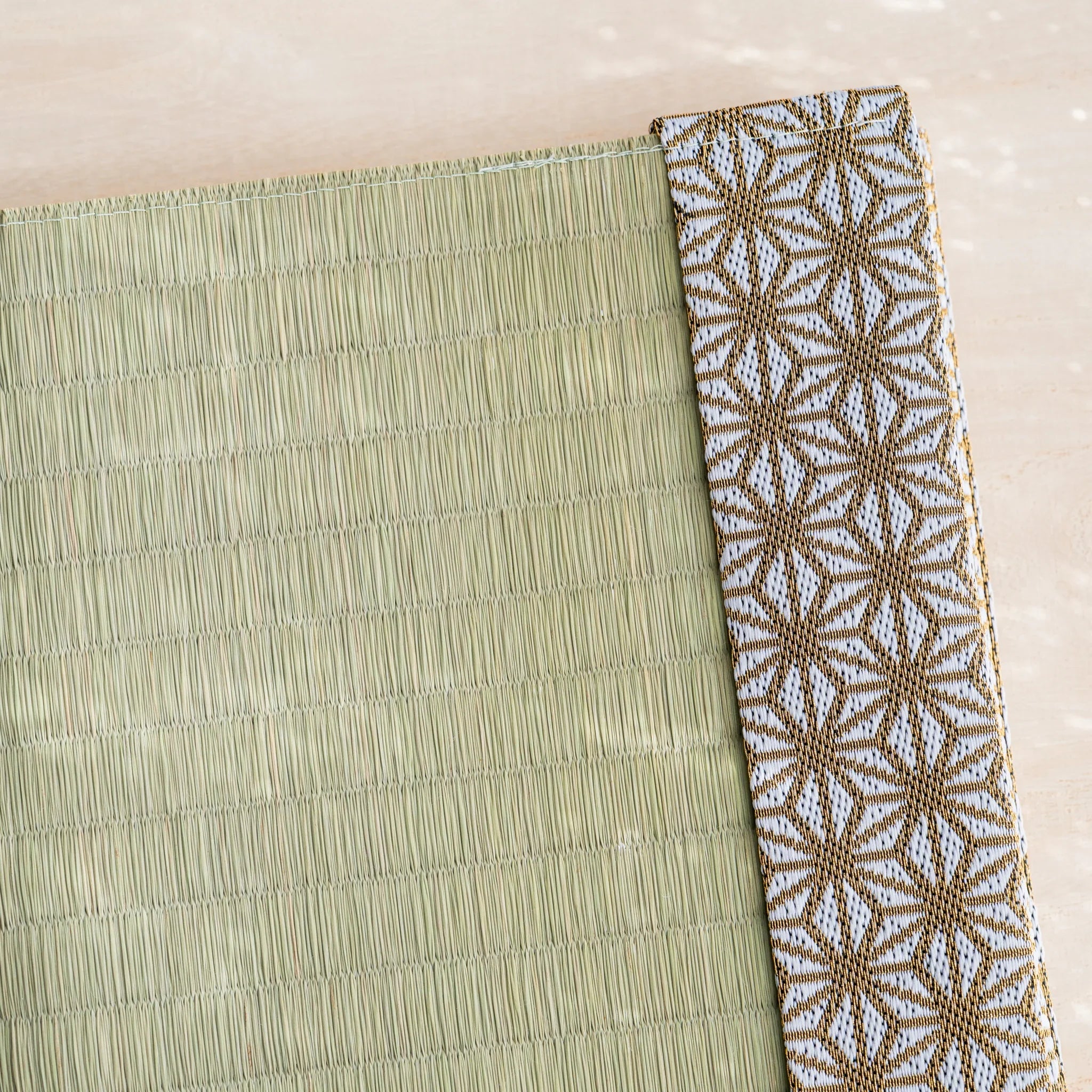 Close-up of gold and white Japanese hemp leaf brocade band beside woven green rush straw at the cover corner