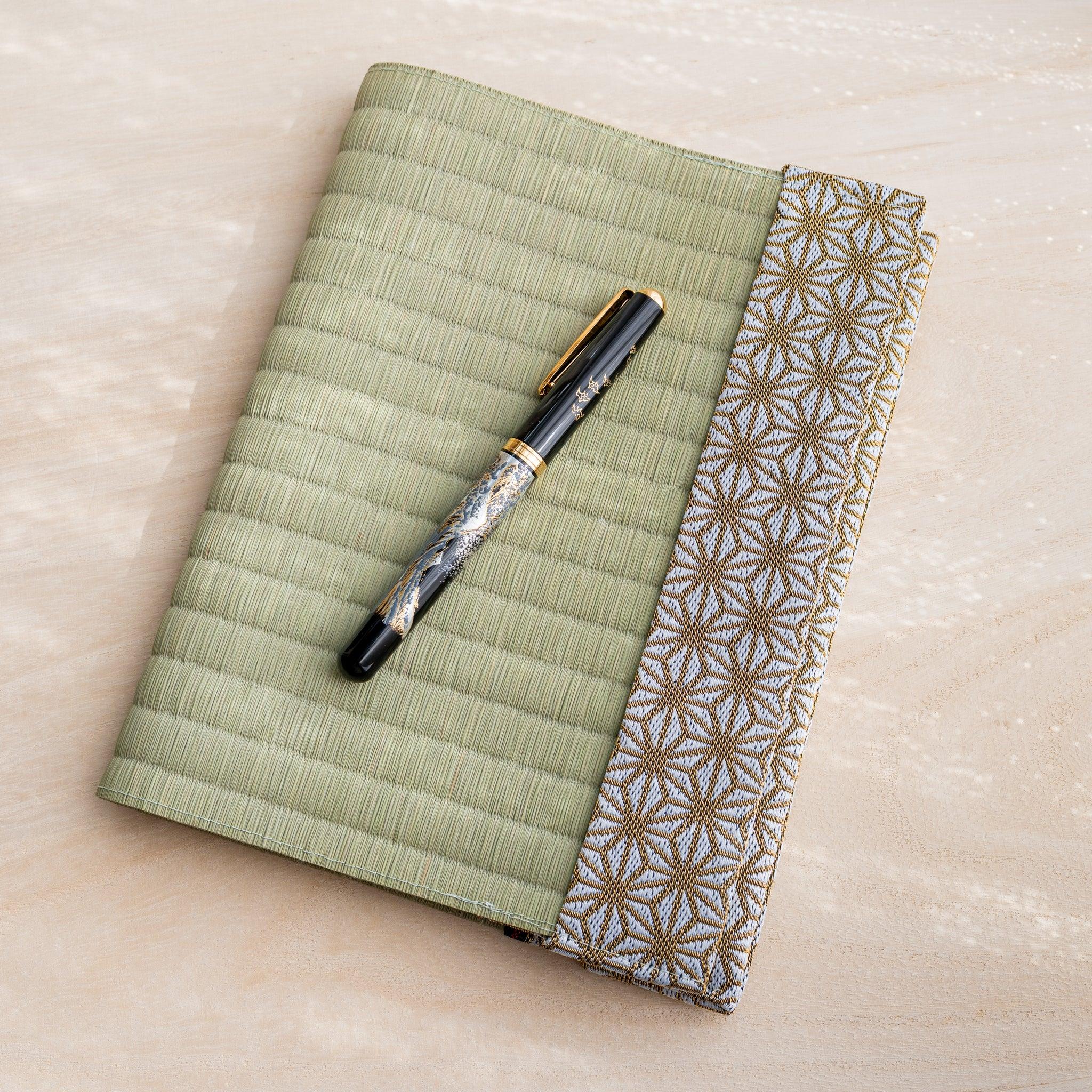 Black and gold fountain pen resting on closed tatami book cover with gold and white hemp leaf pattern fabric band