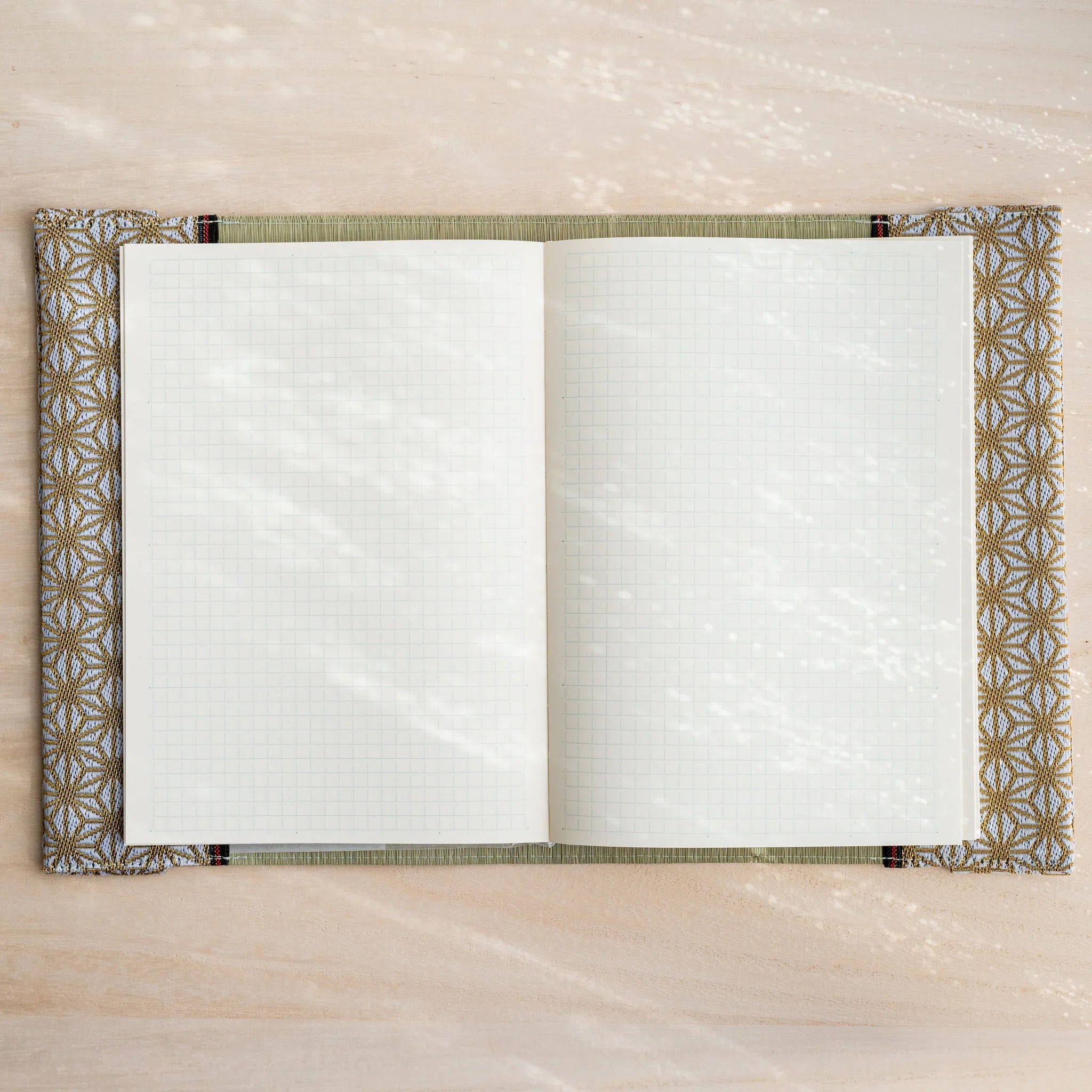 Tatami book cover open flat with cream grid notebook pages, gold and white hemp leaf fabric edges both sides