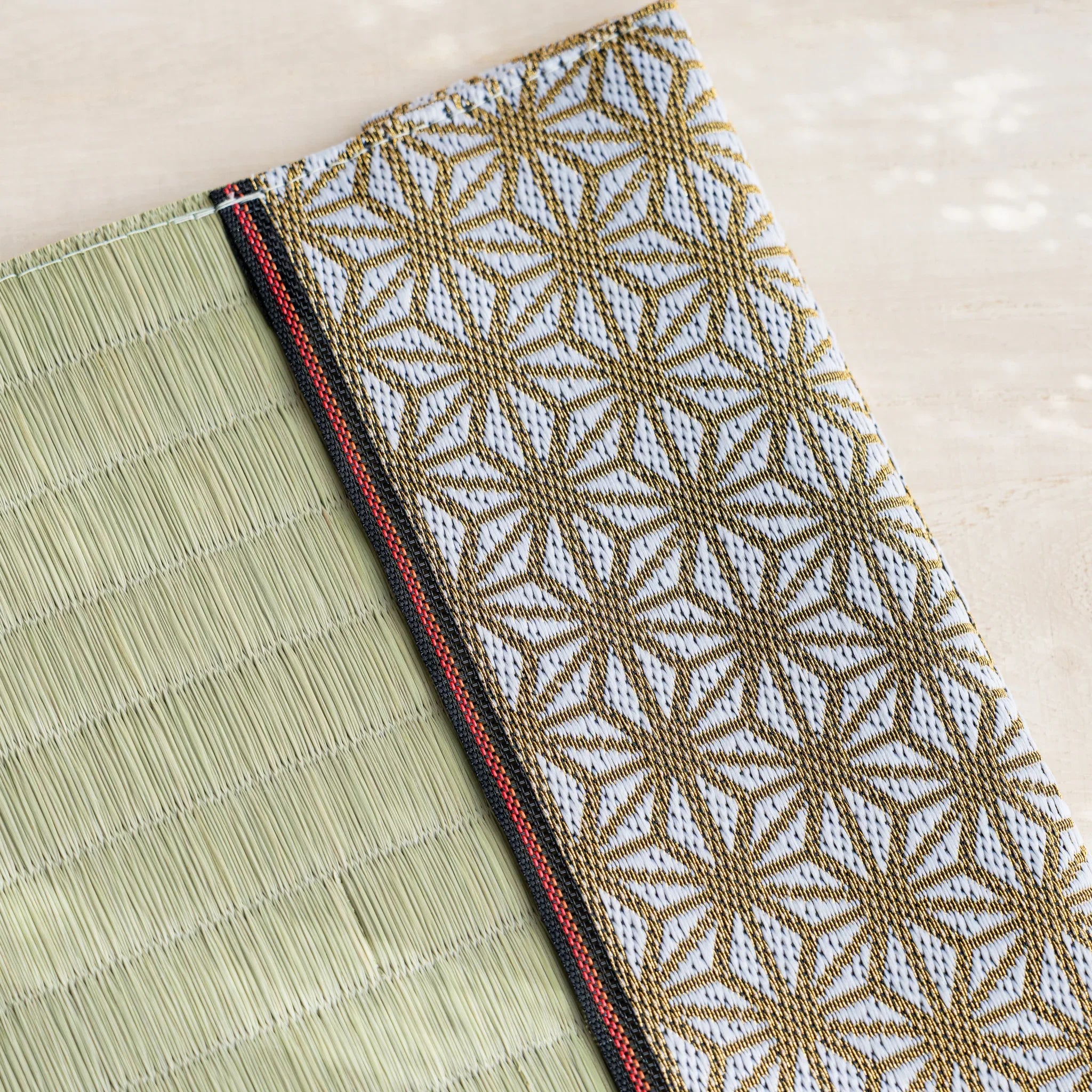 Close-up of gold and white Japanese hemp leaf brocade band with red and black striped trim beside green rush straw