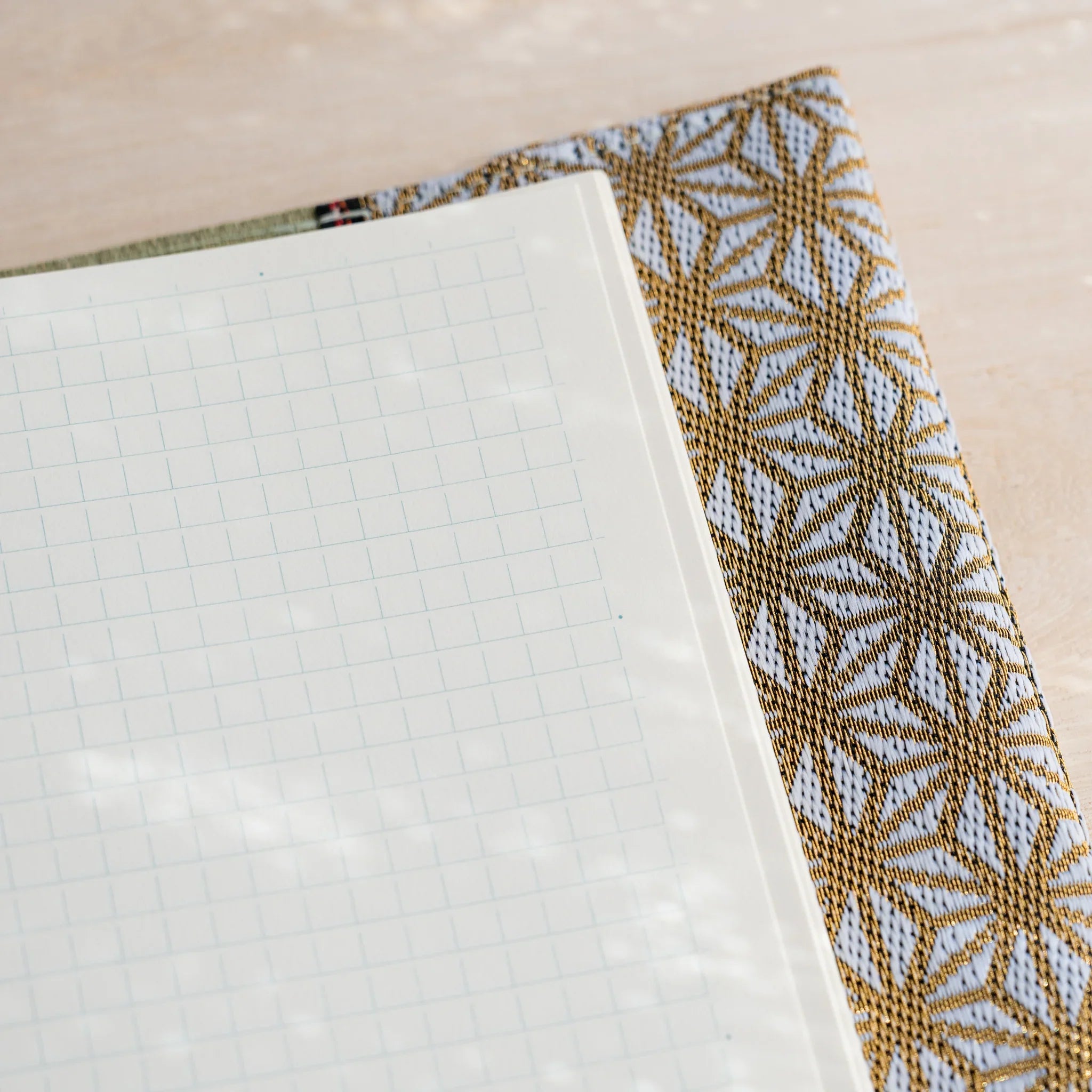 Corner close-up of a cream grid notebook page inside the tatami cover with gold and white hemp leaf fabric flap