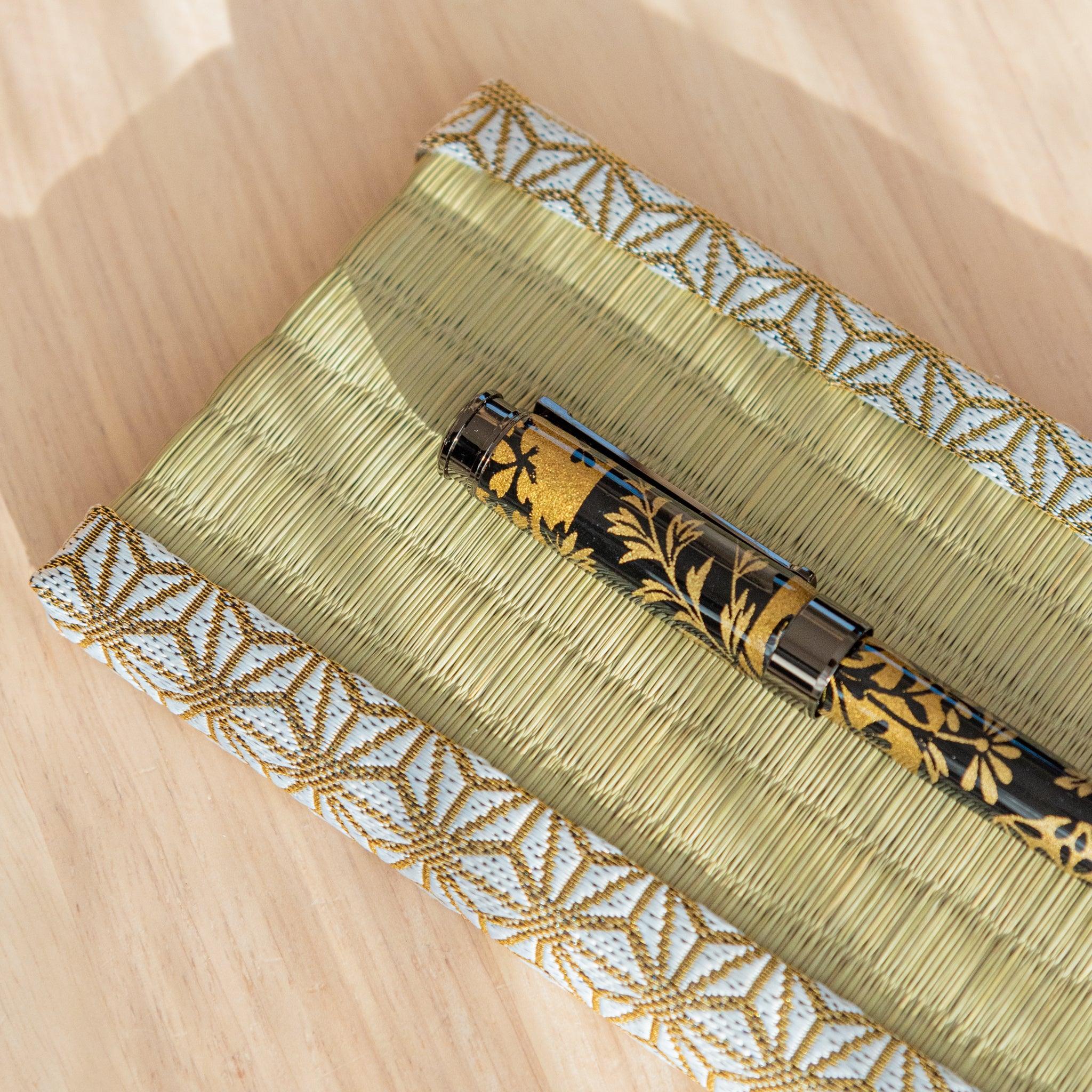 A black and gold Japanese stationery fountain pen on a tatami-style pen tray with a golden ink bottle nearby.  