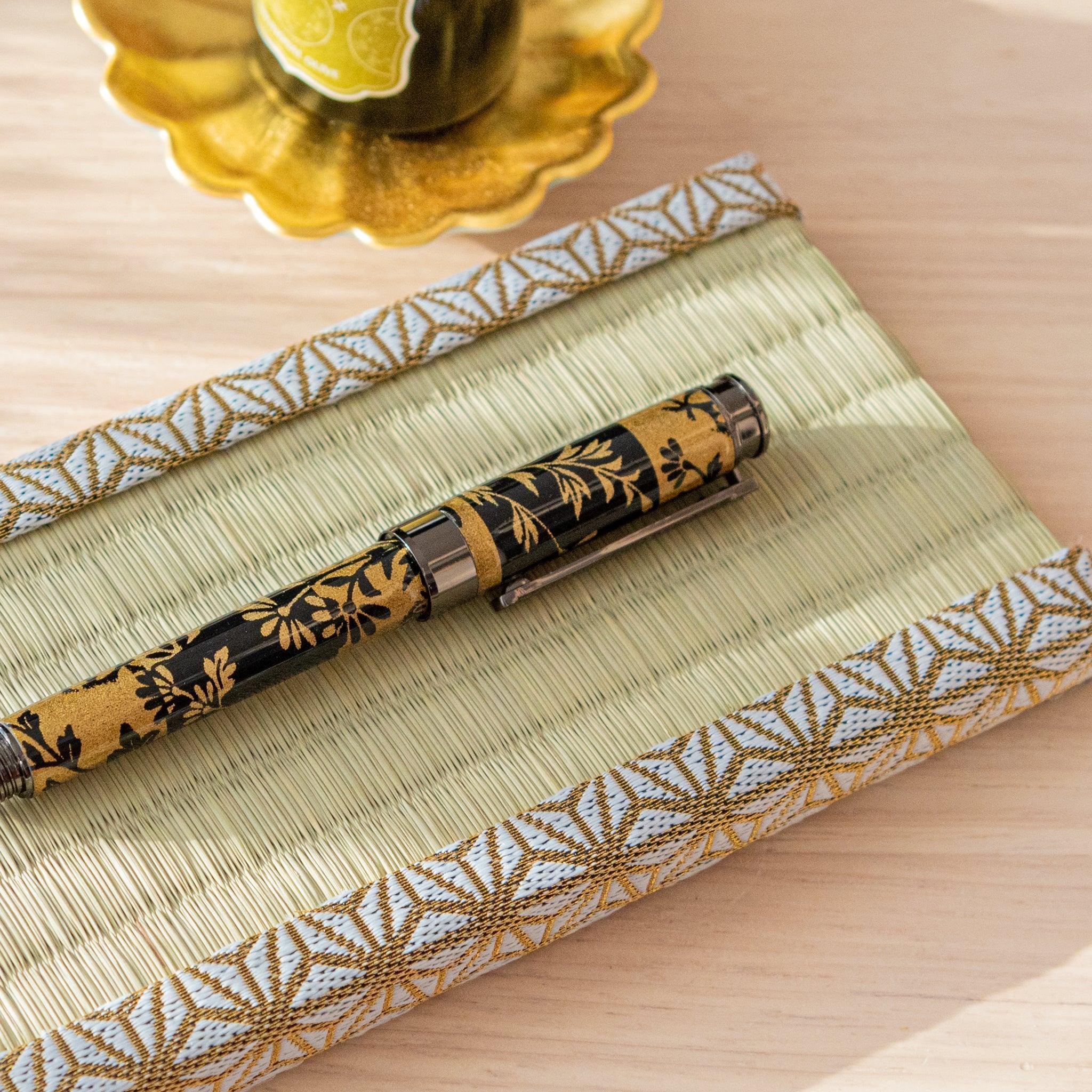 A tatami-style pen tray with gold and white trim placed on a wooden surface under natural light.  