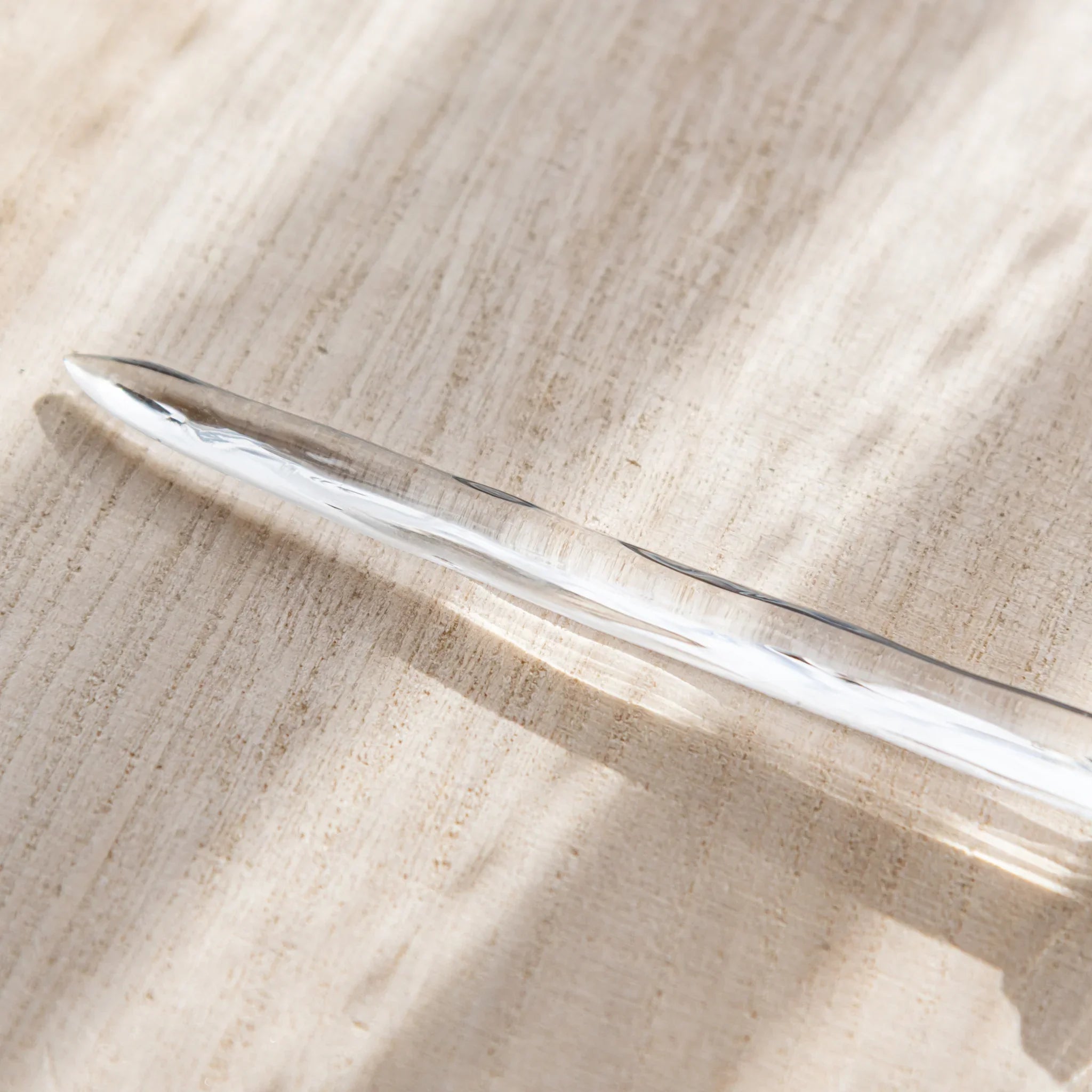 Clear Hikari glass letter opener resting on a sunlit wooden desk, featuring Japanese Stationery.
