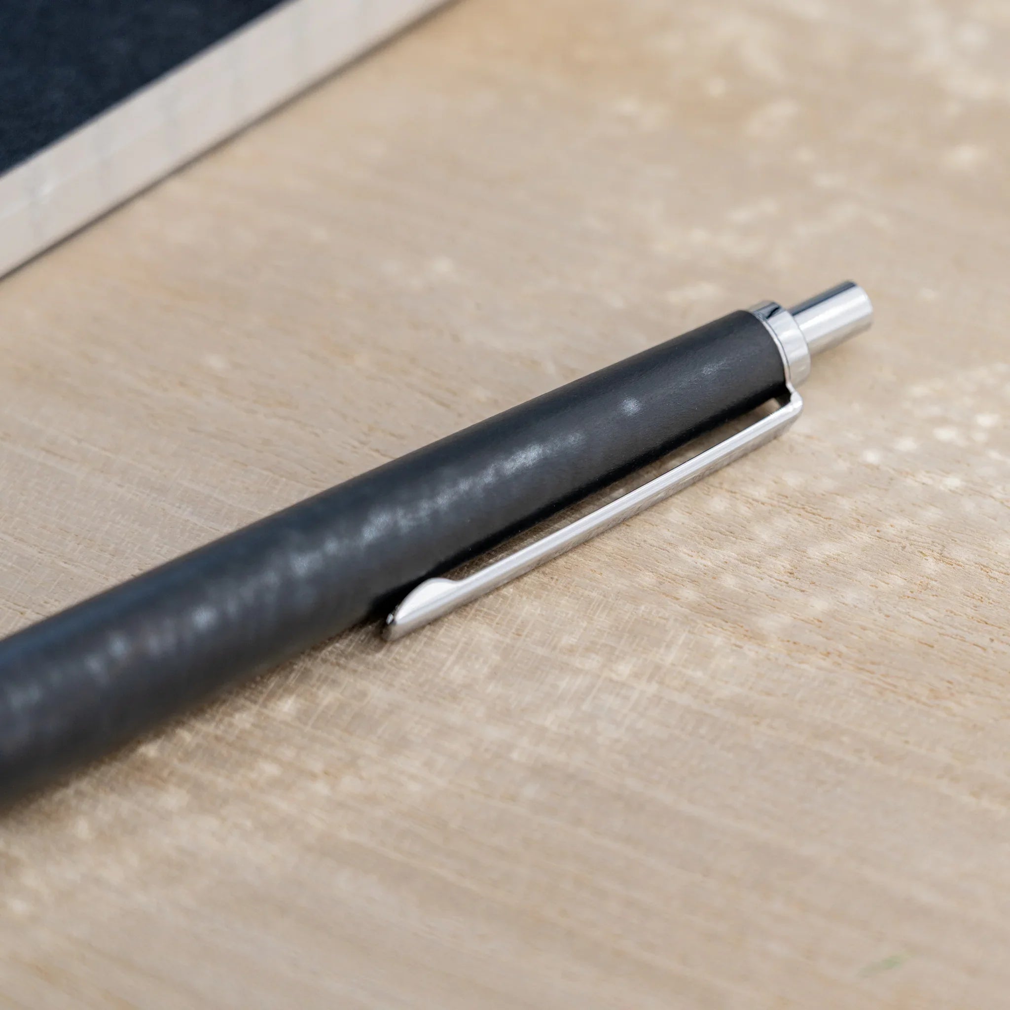 Charcoal black horse chestnut wood urushi ballpoint pen, close-up of lower barrel and silver cone tip, Japanese wood