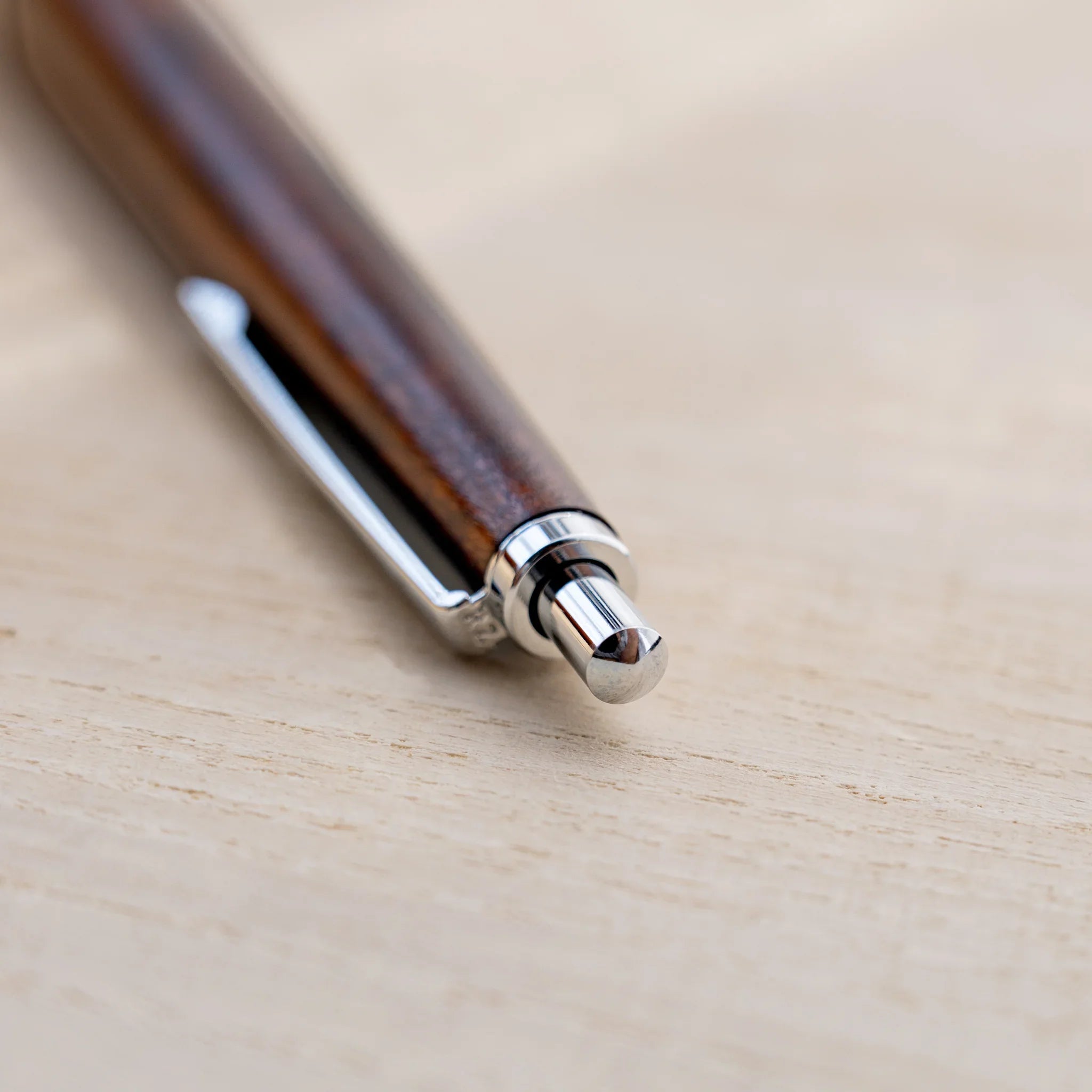 Amber-brown horse chestnut wood urushi ballpoint pen, close-up of lower barrel and silver cone tip, Japanese wood