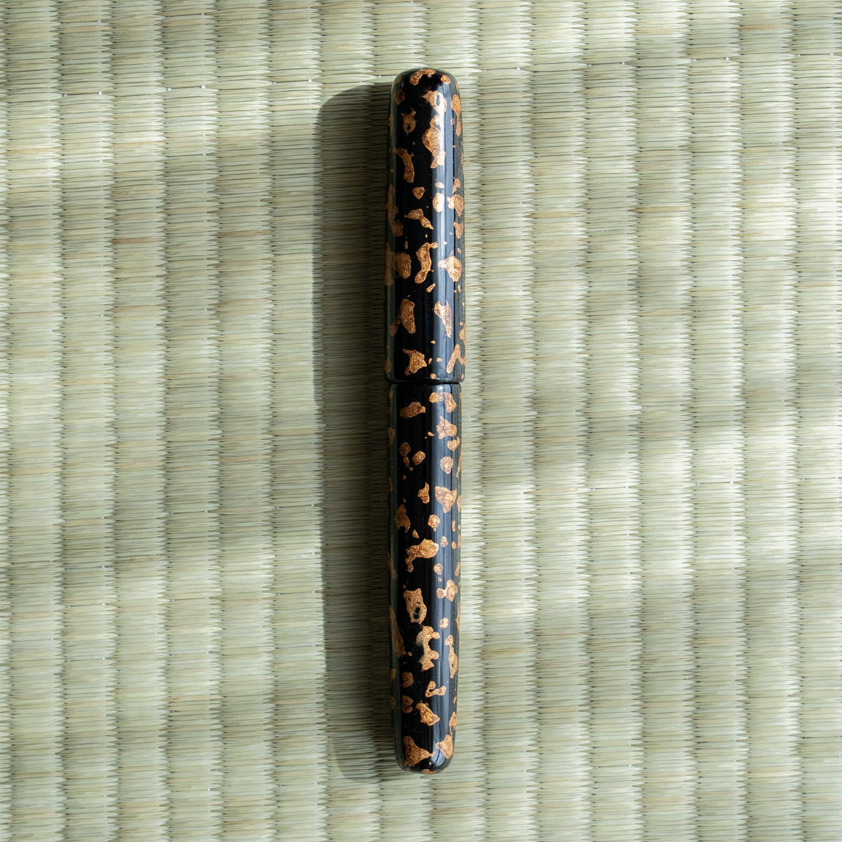 Hoshizukiyo Tsugaru-nuri urushi fountain pen, capped, glossy black lacquer with gold flecks, on a tatami mat