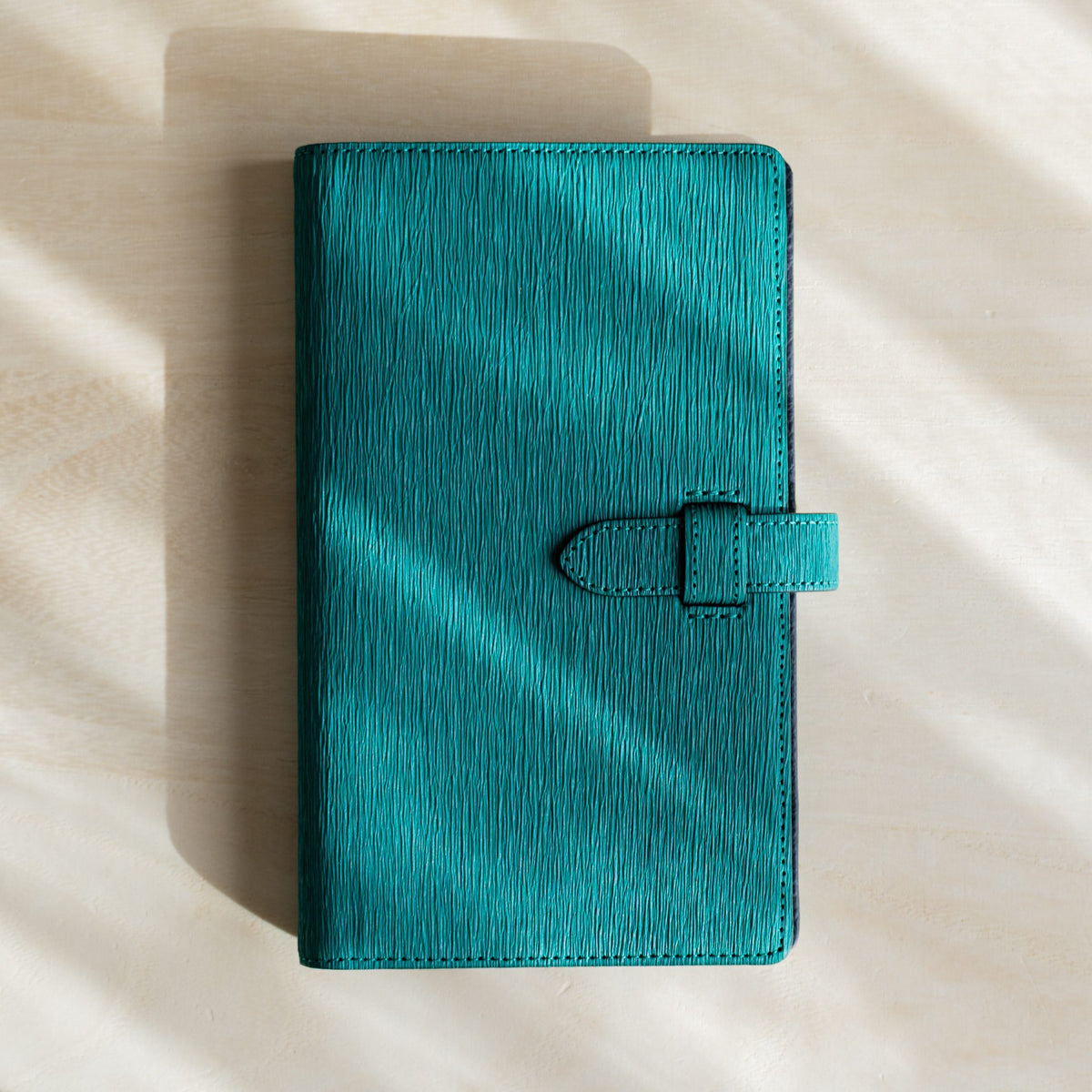 Ise Gikakushi paper leather planner, Bible size in teal, closed with creased cover texture and stitched belt strap