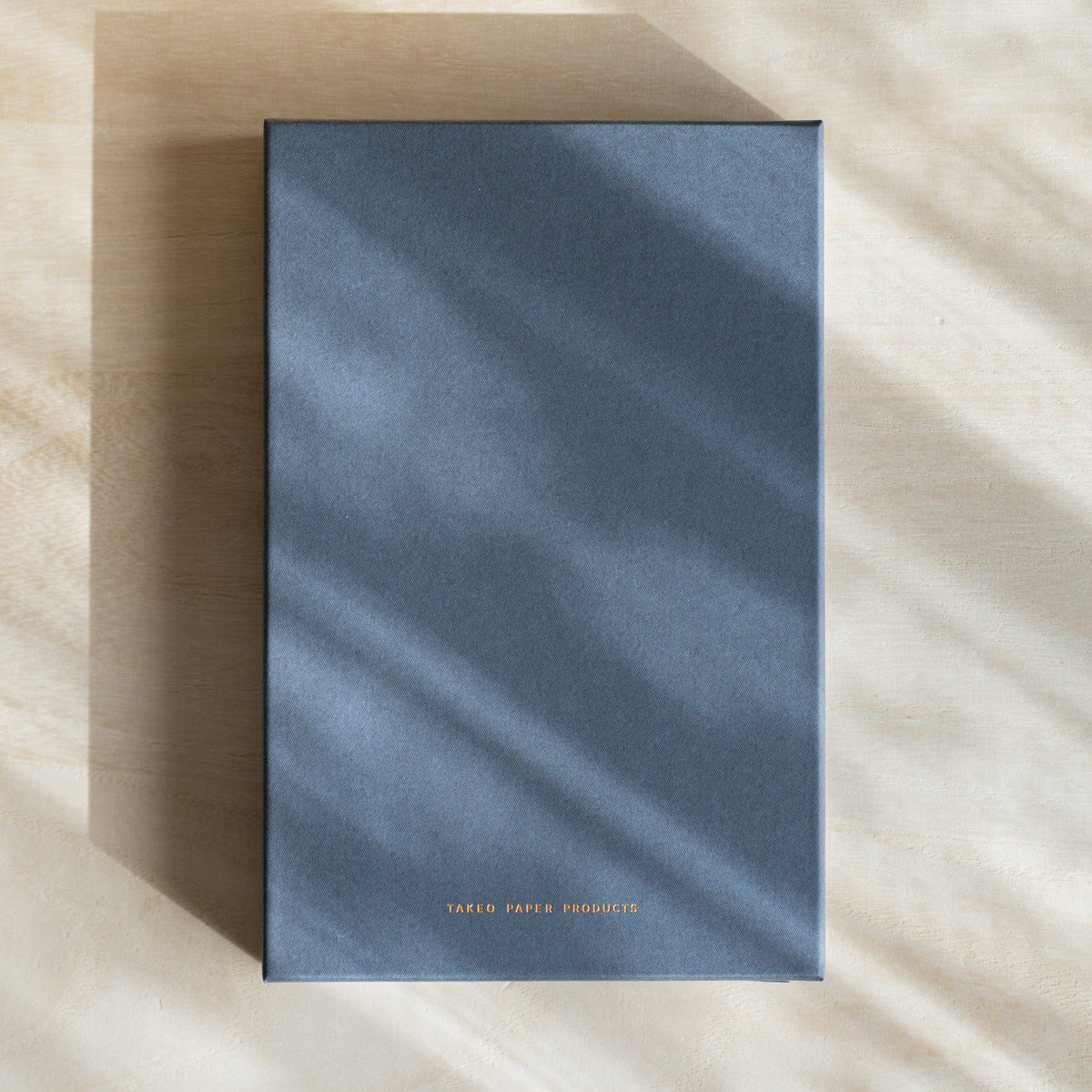 Closed gray TAKEO PAPER PRODUCTS gift box with gold logo text