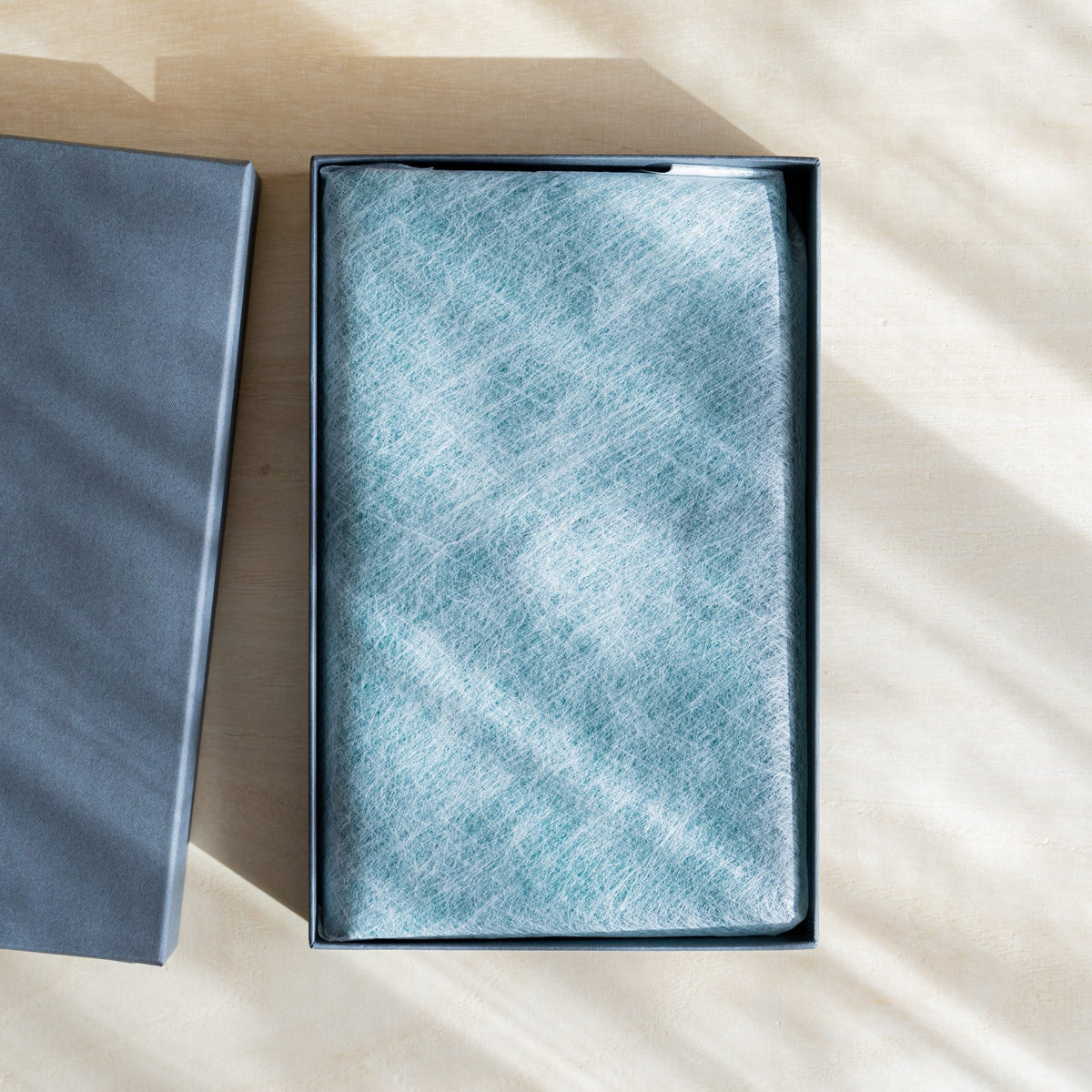 Gift box opened with the planner wrapped in white nonwoven cloth, lid set aside
