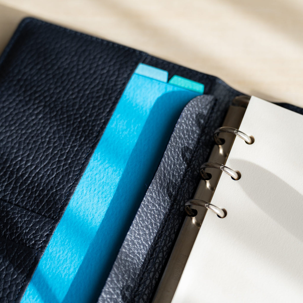 Sky blue and turquoise sheets in the inner pocket of the navy planner beside cream pages on rings