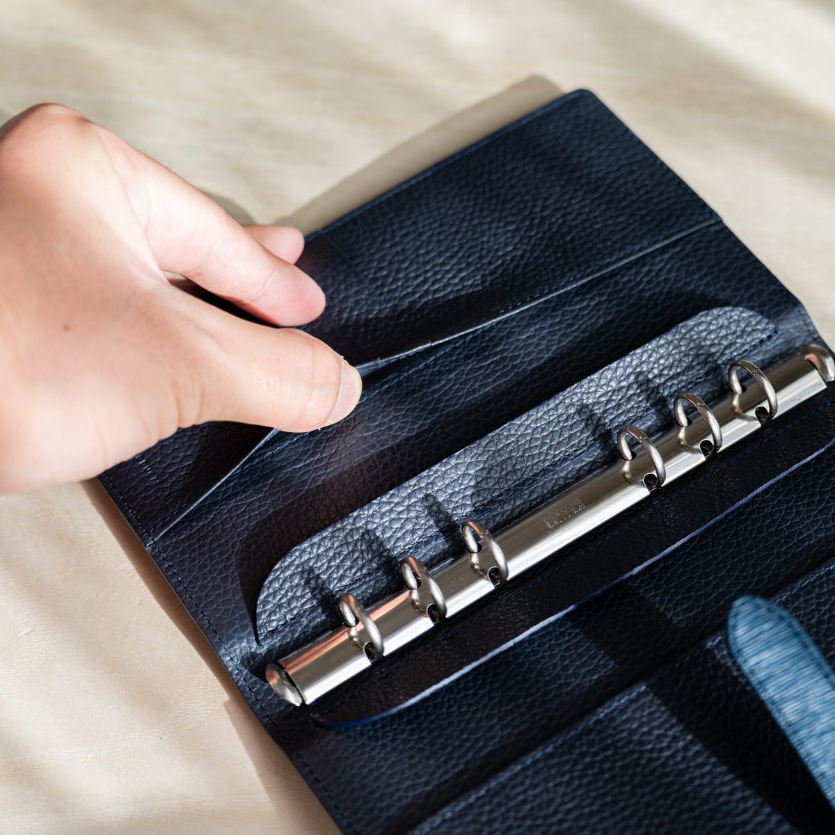 Hand opening the inner pocket flap beside the binder rings in the navy leather planner