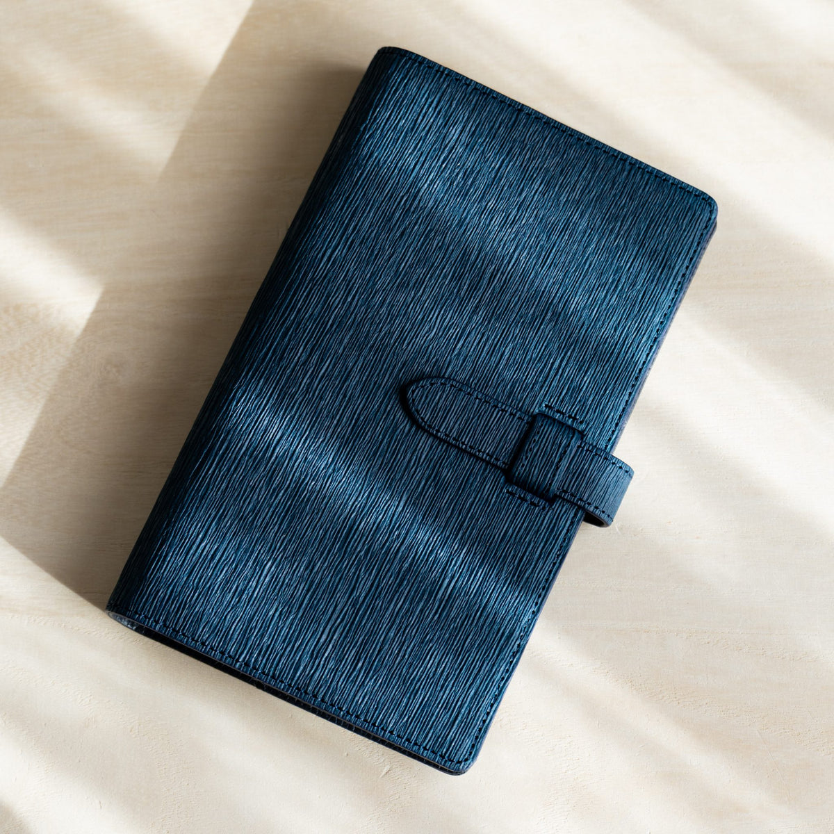 Navy Ise Gikakushi paper leather planner at an angle showing crease texture and strap