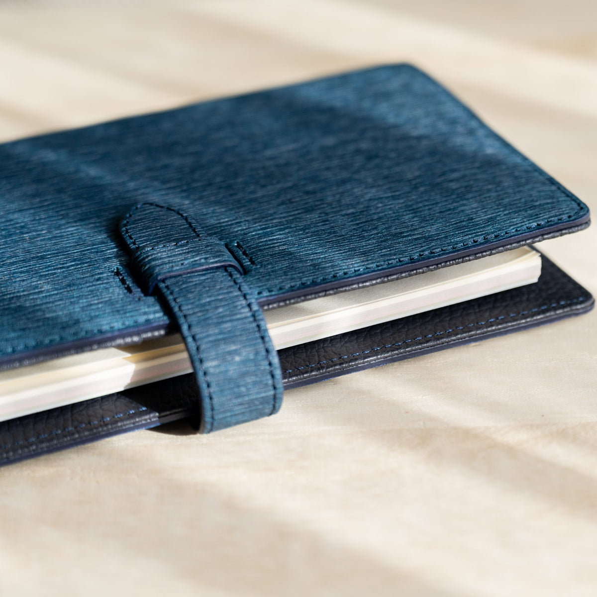 Closed navy paper leather planner with the strap fastened and page edges showing