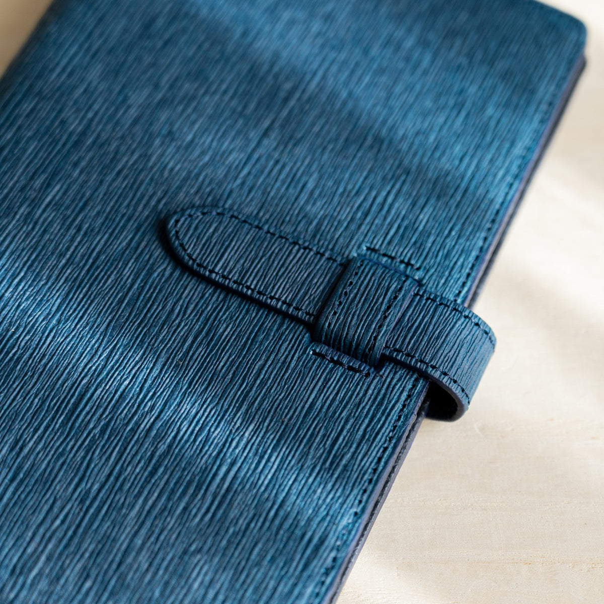 Close-up of the navy paper leather cover creases and stitched strap closure