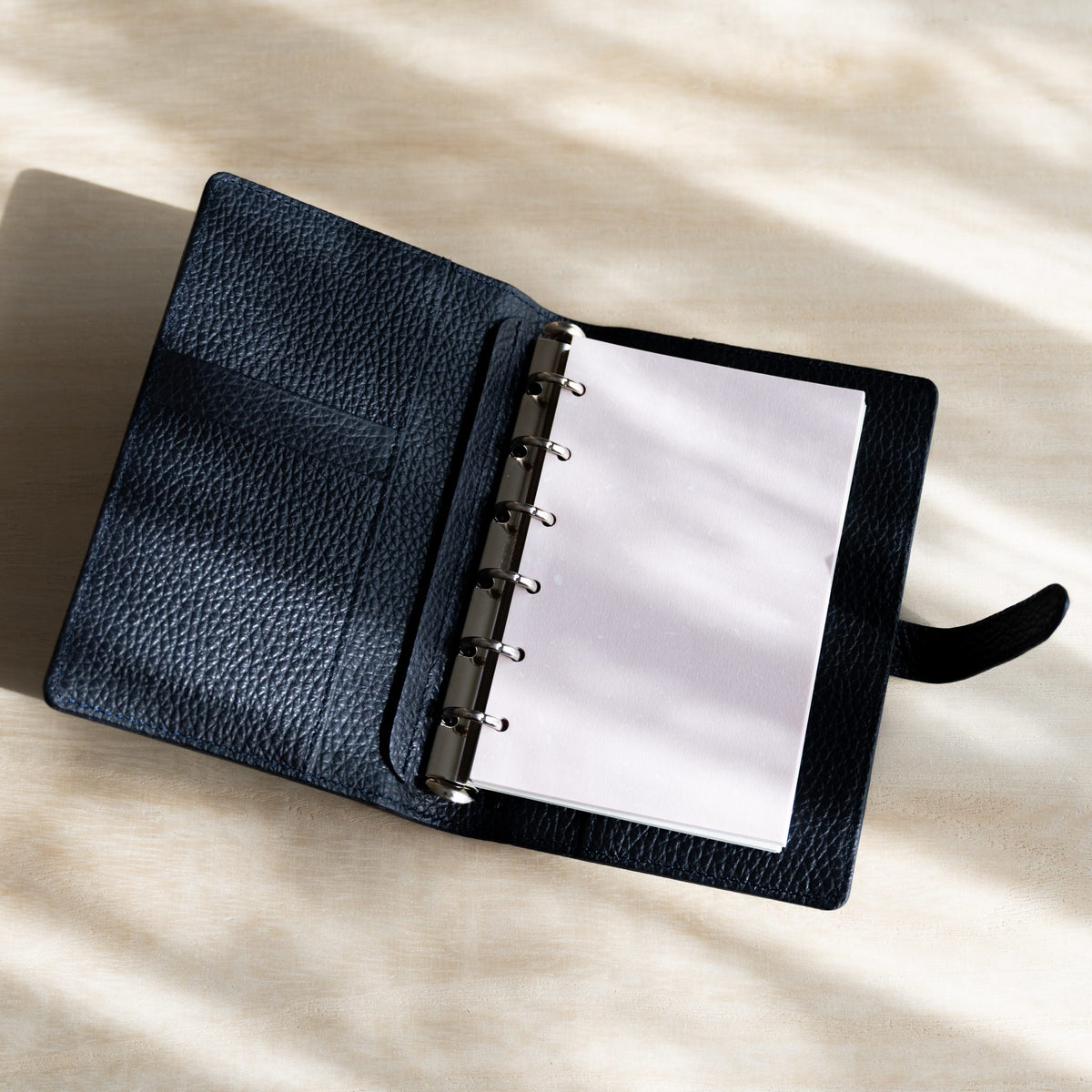 Open navy planner with white pages on silver rings and navy grained leather pockets