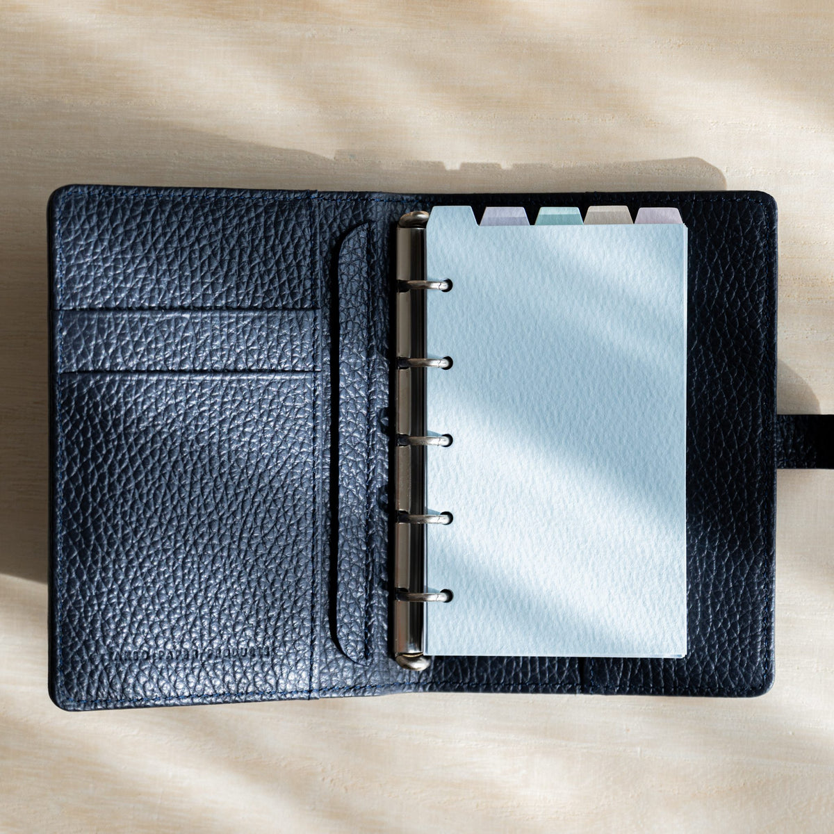 Open planner with navy leather interior, card slots and a pale blue tabbed divider on silver rings