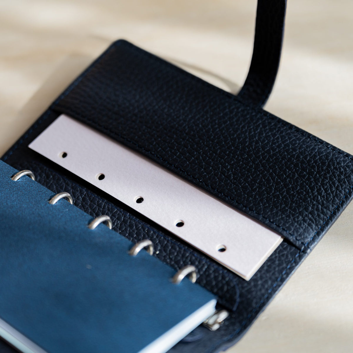 Pale pink hole-punched strip in the inner pocket beside dark blue pages on silver rings