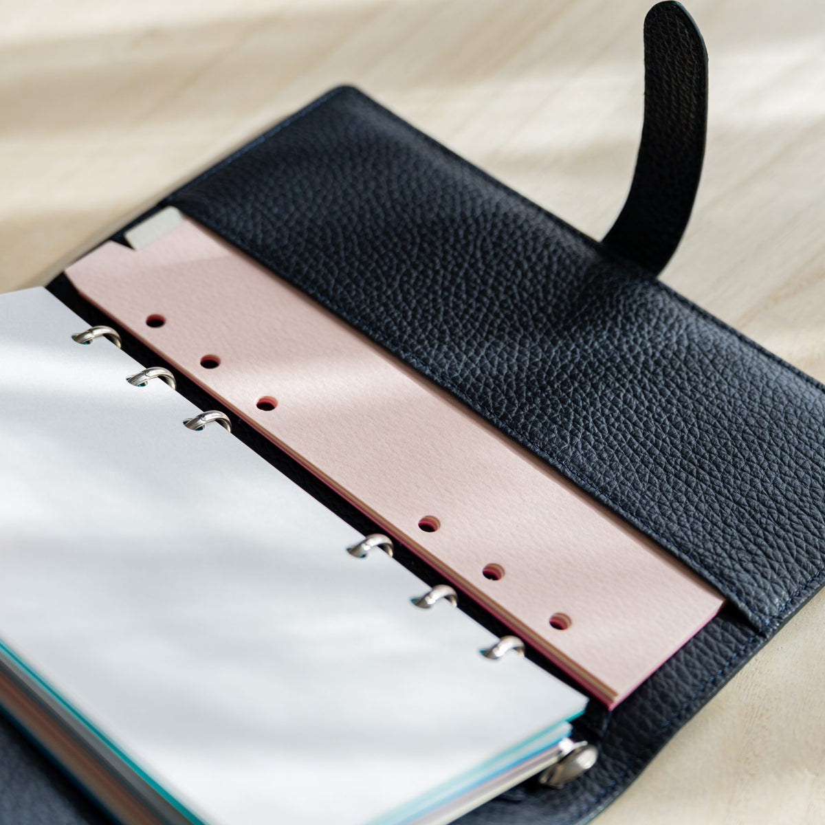 Pale pink hole-punched strip and white pages in the open navy planner, strap raised
