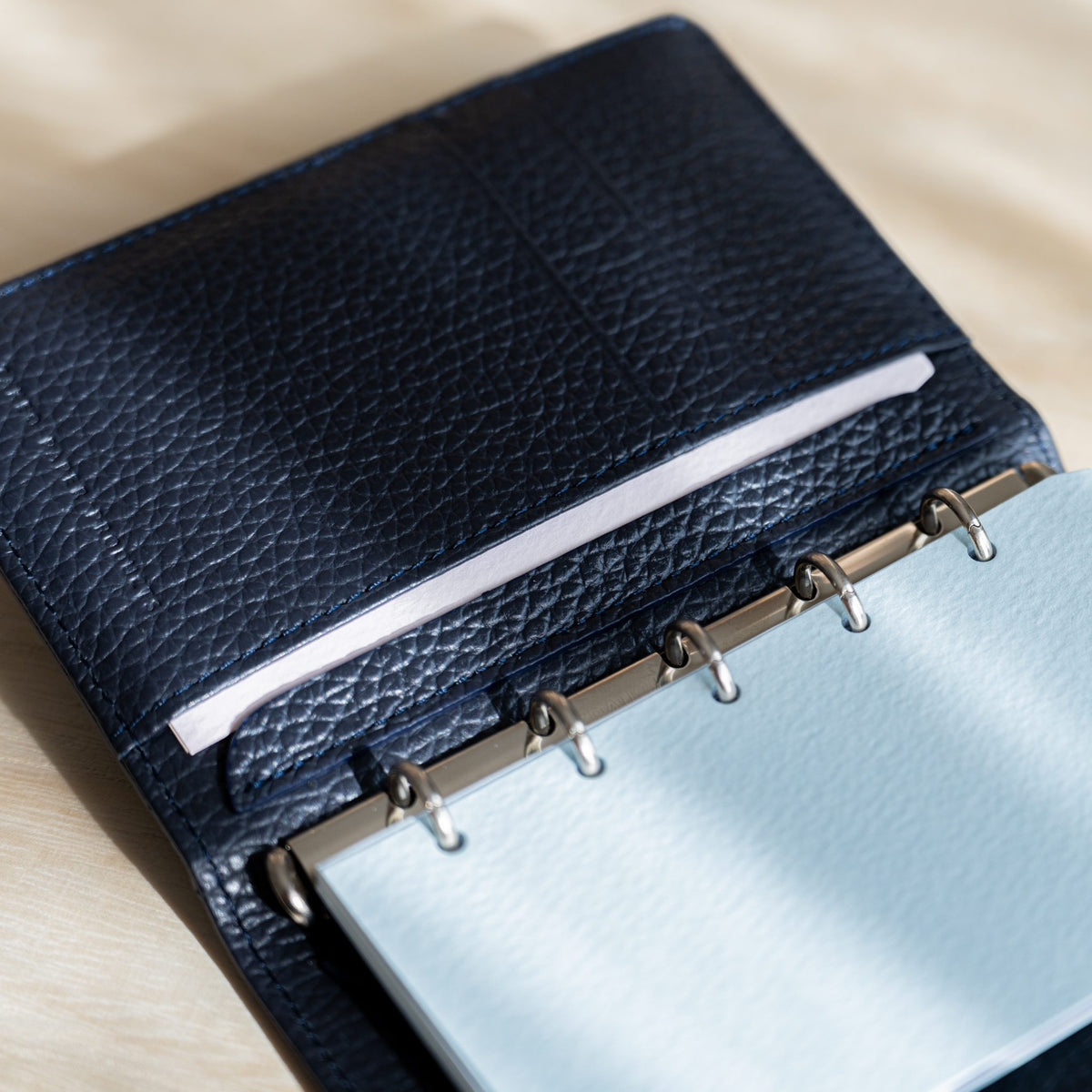 Pale pink strip in the navy leather pocket above pale blue pages on the rings