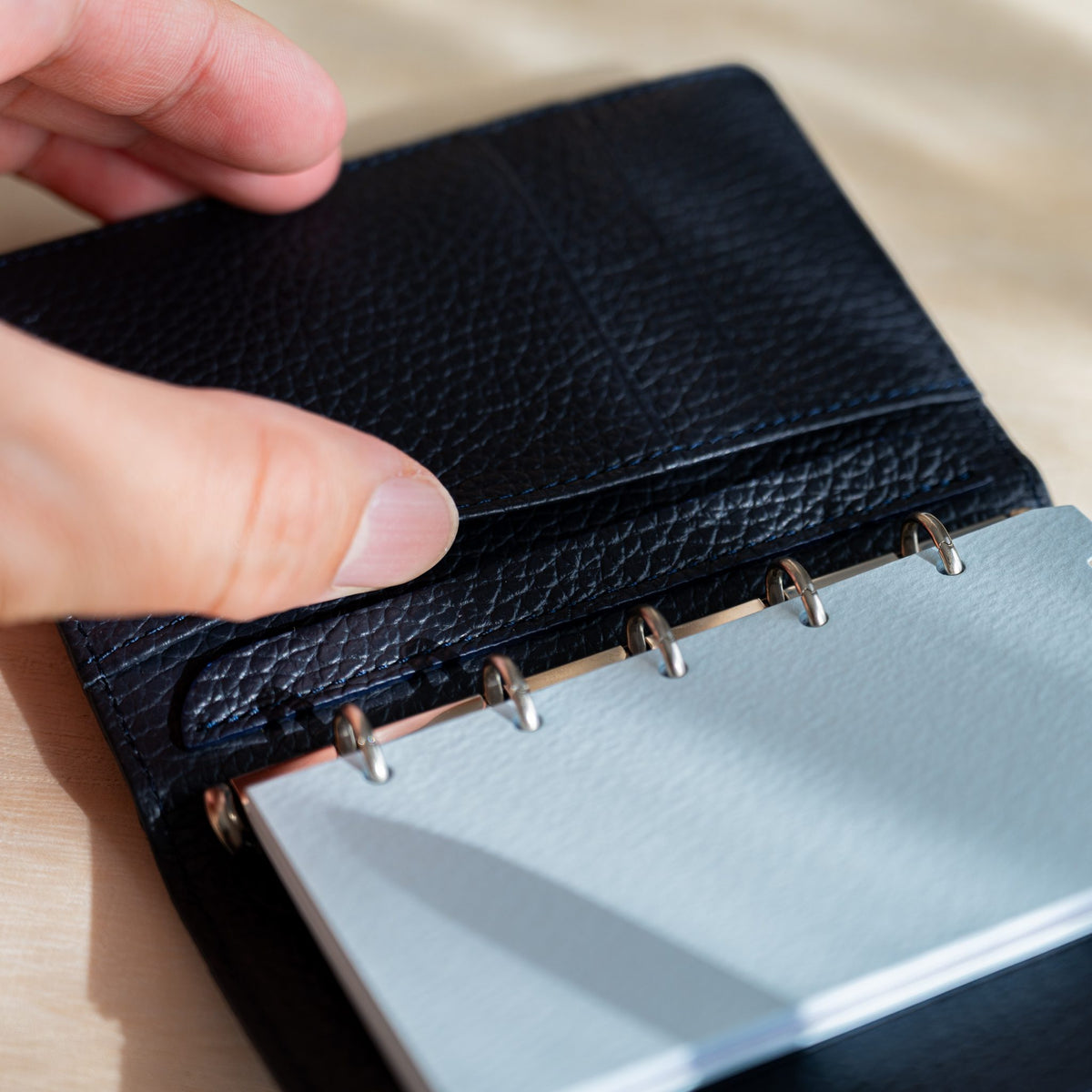 Fingers opening the navy leather pocket over pale blue pages on silver rings