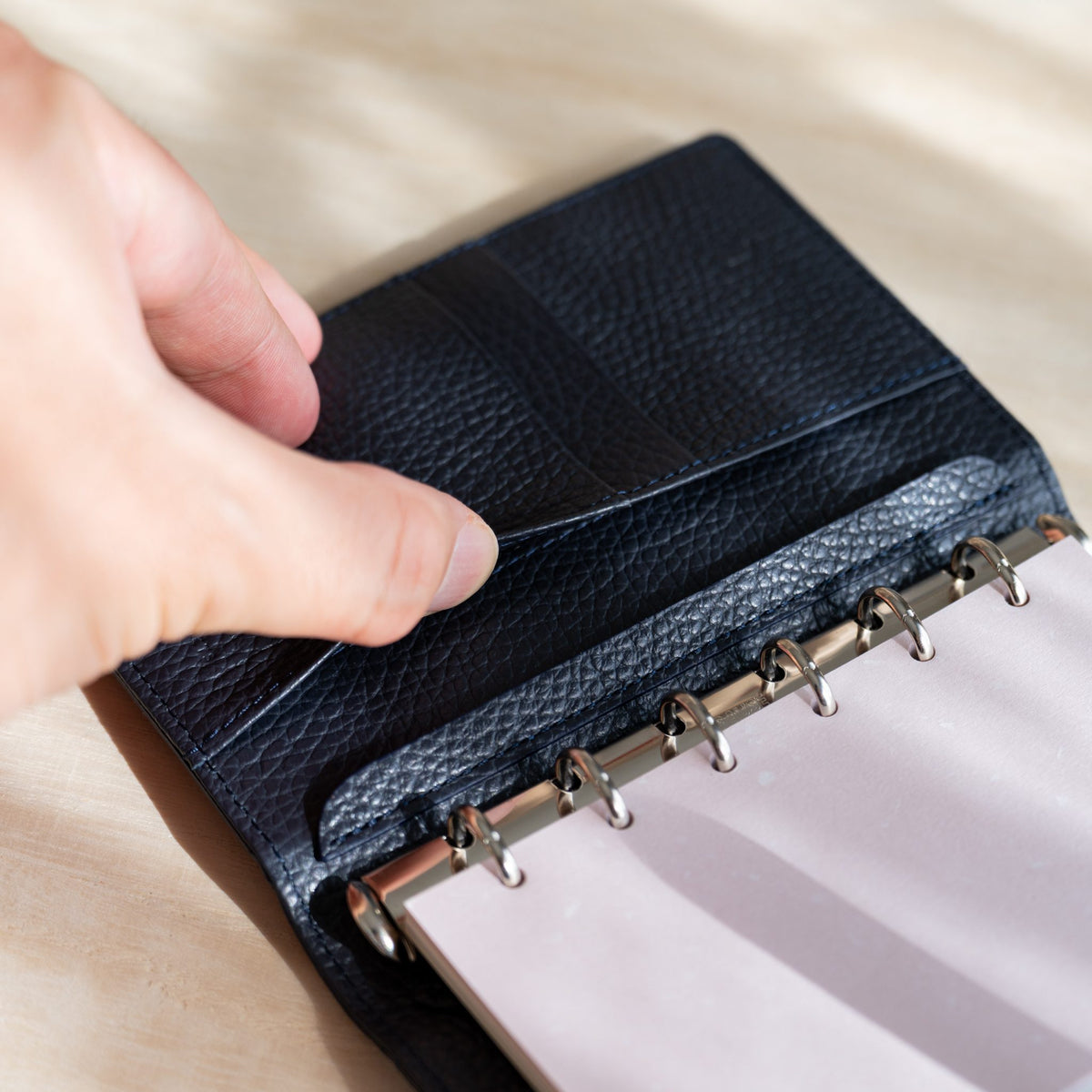 Hand opening the inner pocket of the navy leather lining above white pages on the rings