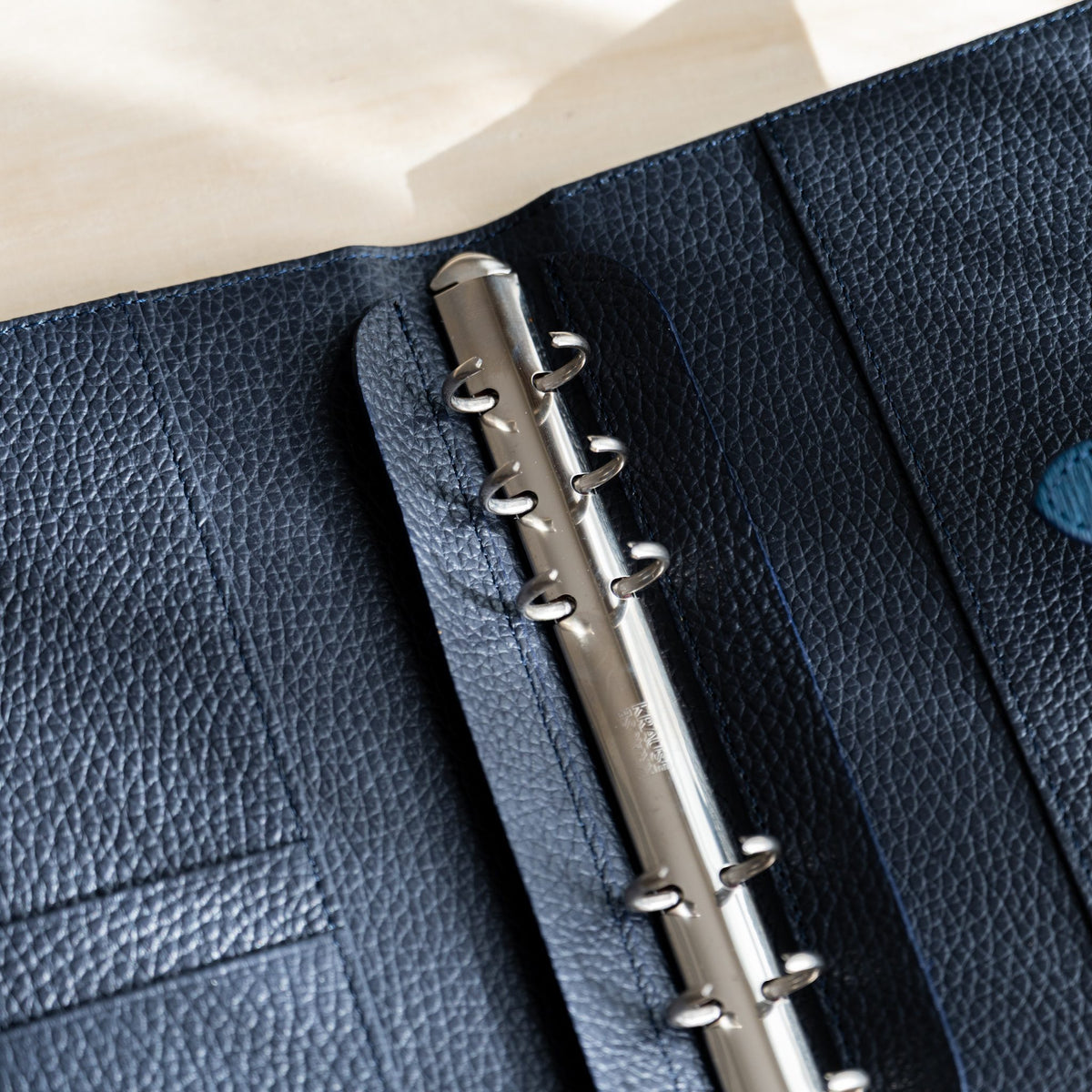 Silver ring mechanism and card slots on the navy grained leather lining of the open planner