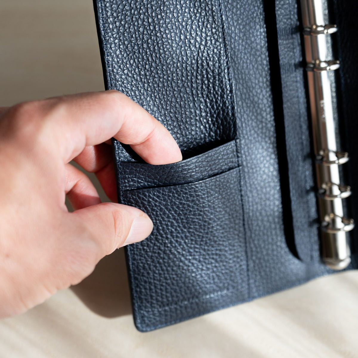 Hand opening a slip pocket on the navy grained leather inside cover of the planner