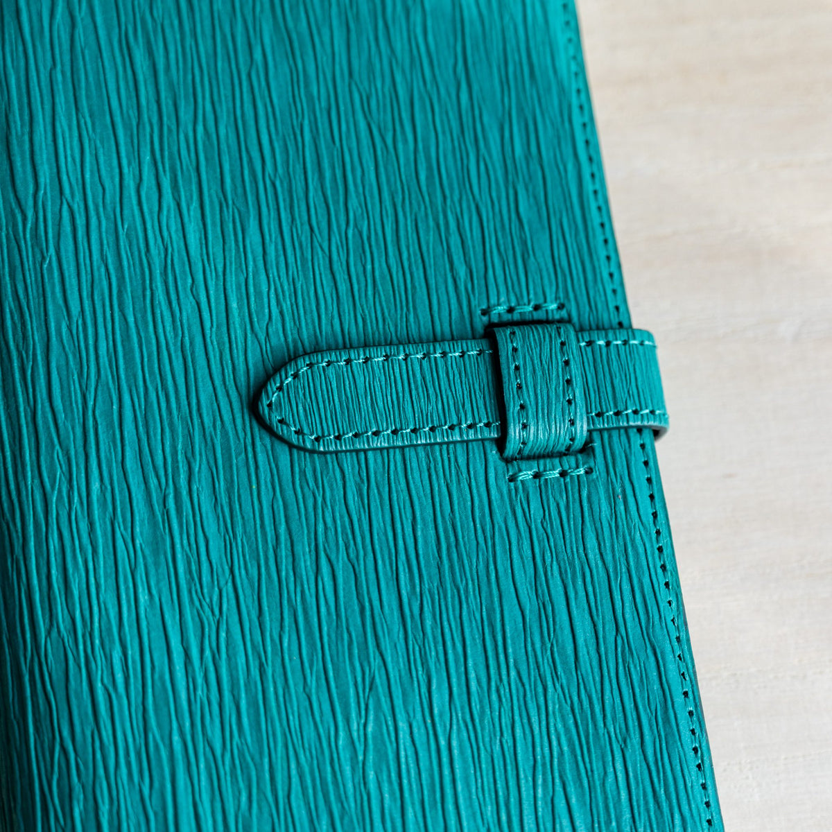 Macro view of deep vertical creases in teal paper leather around the stitched strap
