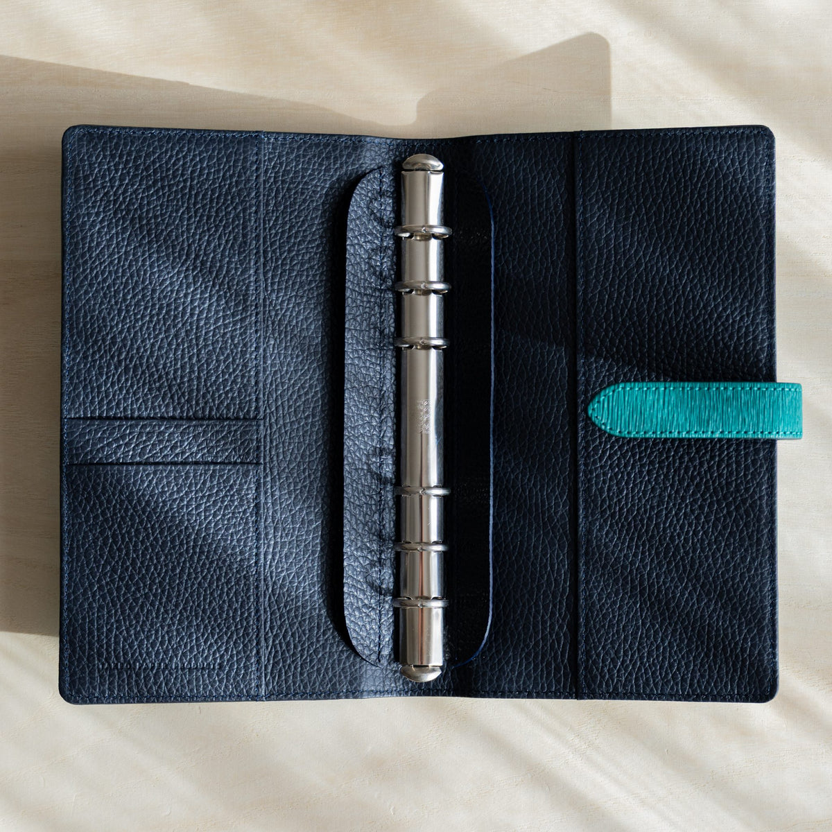 Ise Gikakushi planner opened flat, navy grained leather interior, silver binder rings, card pockets and teal strap