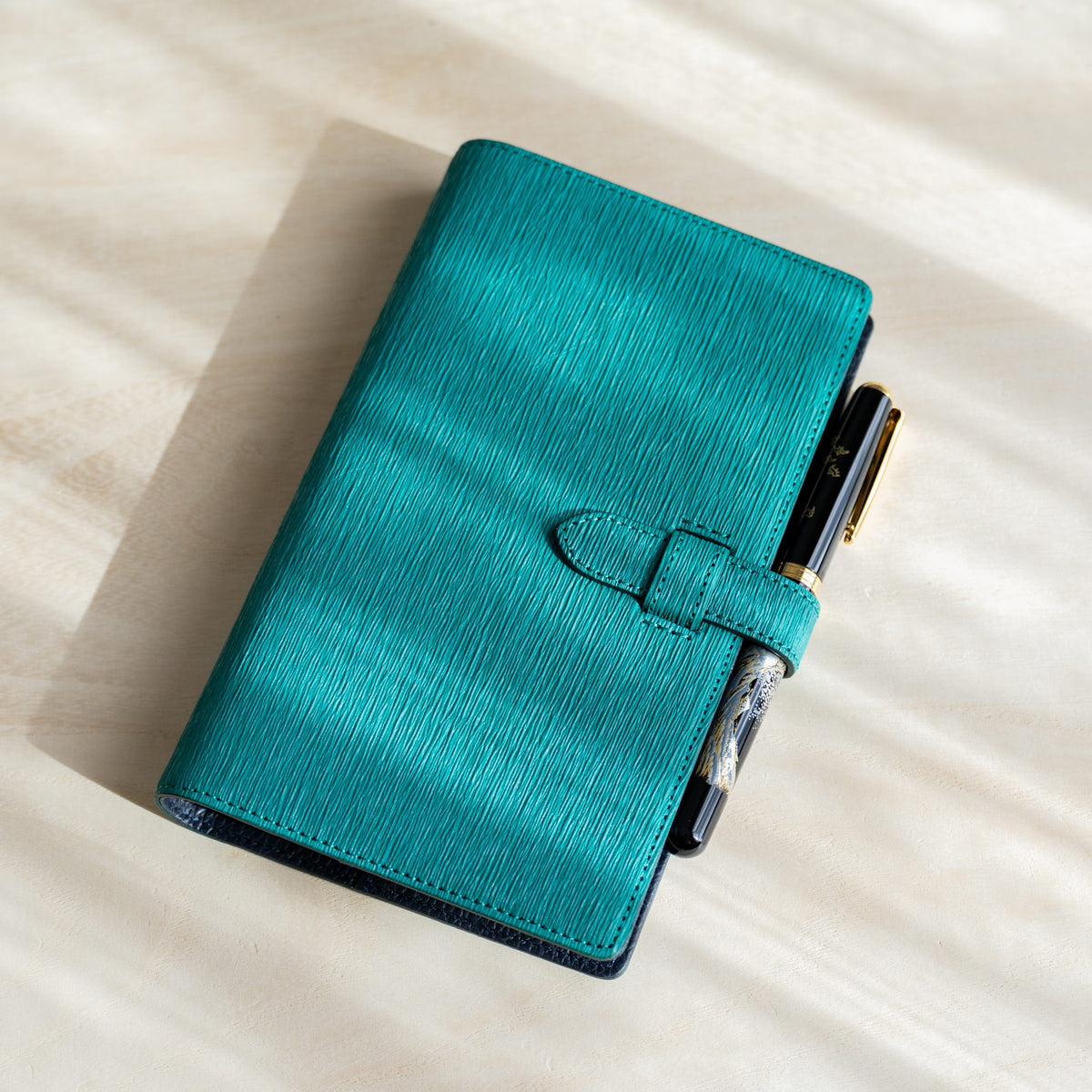 Teal Ise Gikakushi paper leather planner with a fountain pen tucked under the belt strap