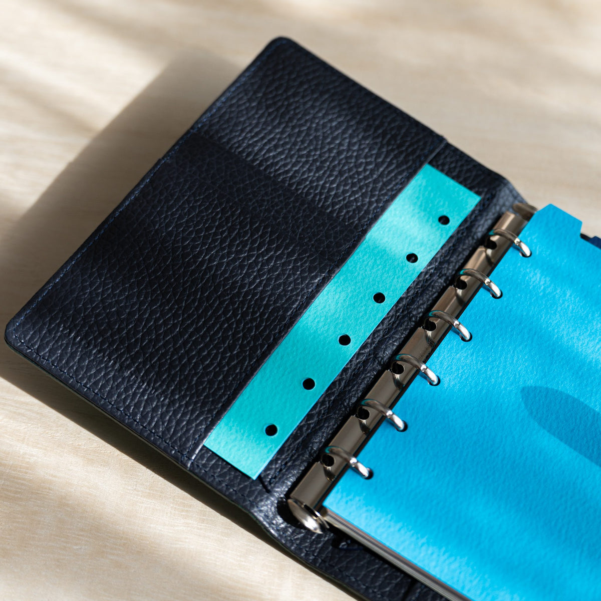 Turquoise hole-punched strip tucked in the navy leather pocket beside blue pages on the rings