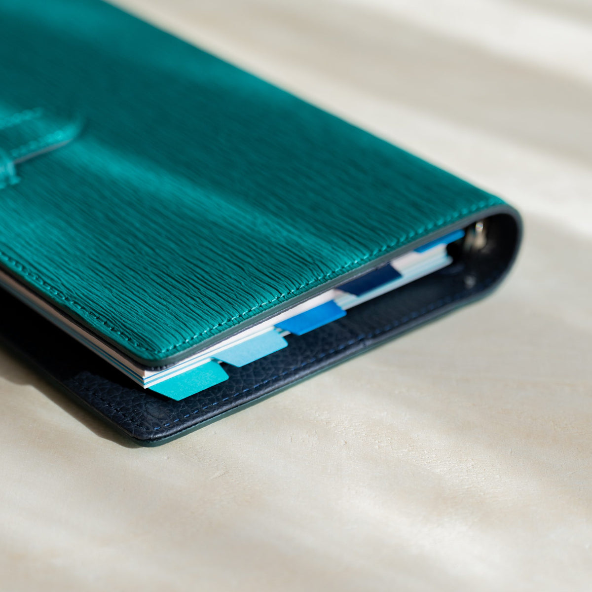 Corner of a closed teal Ise Gikakushi planner showing staggered Mermaid Assorted Blues index tabs