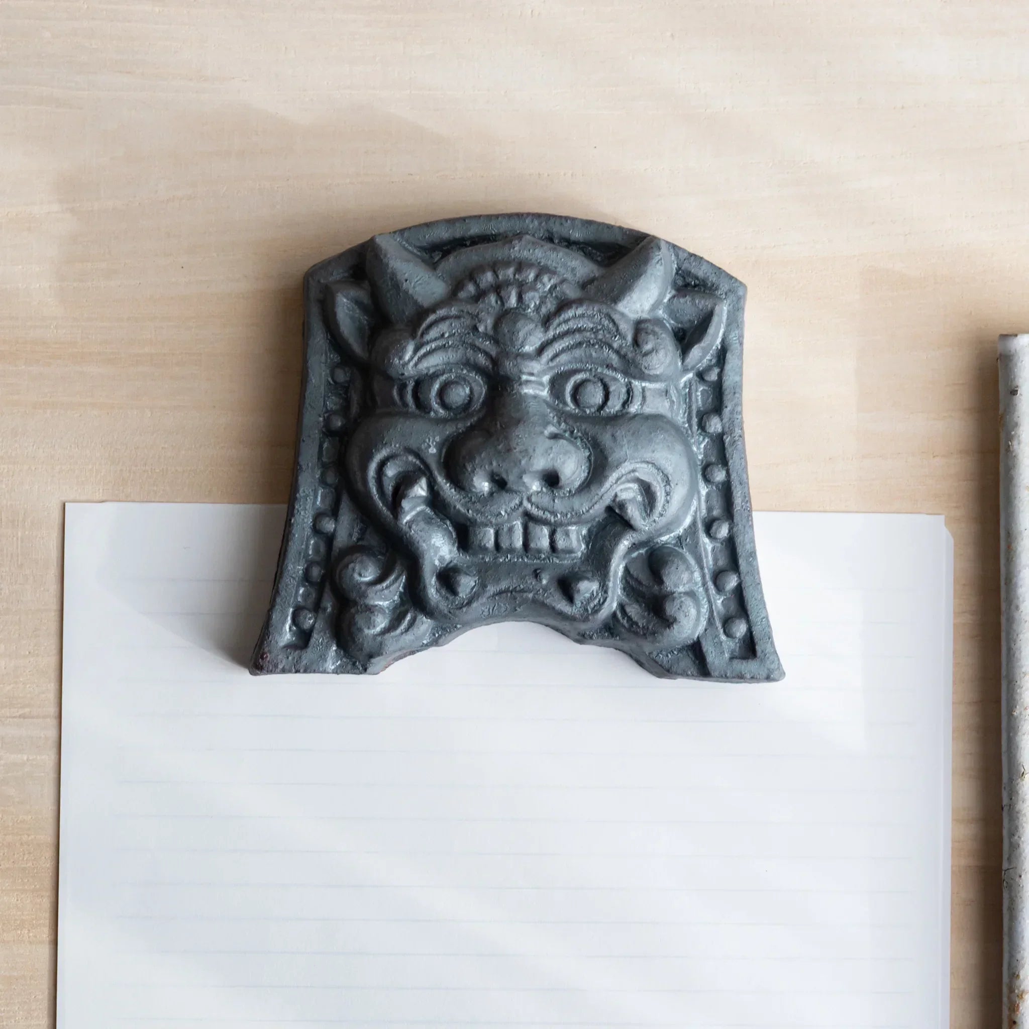 Japanese Paperweight Desk Accessory with resolute oni roof guardian face resting on lined paper, artisan ceramic piece.