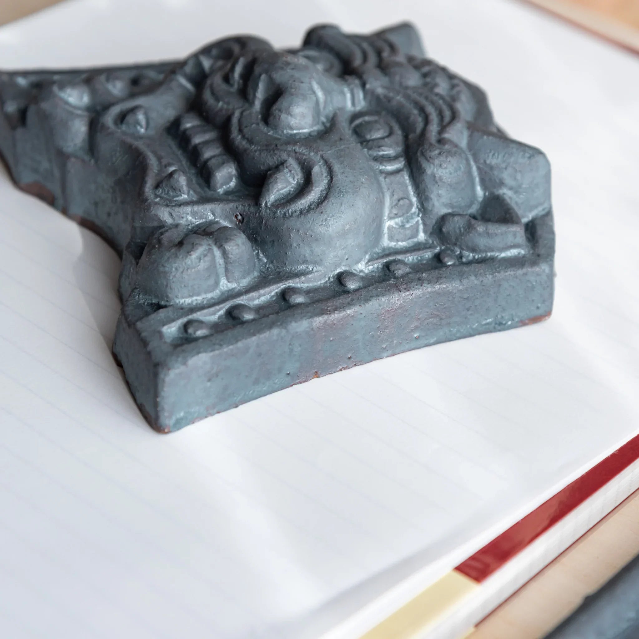 Japanese Paperweight Desk Accessory showing side corner view of resolute oni roof guardian tile on lined paper.